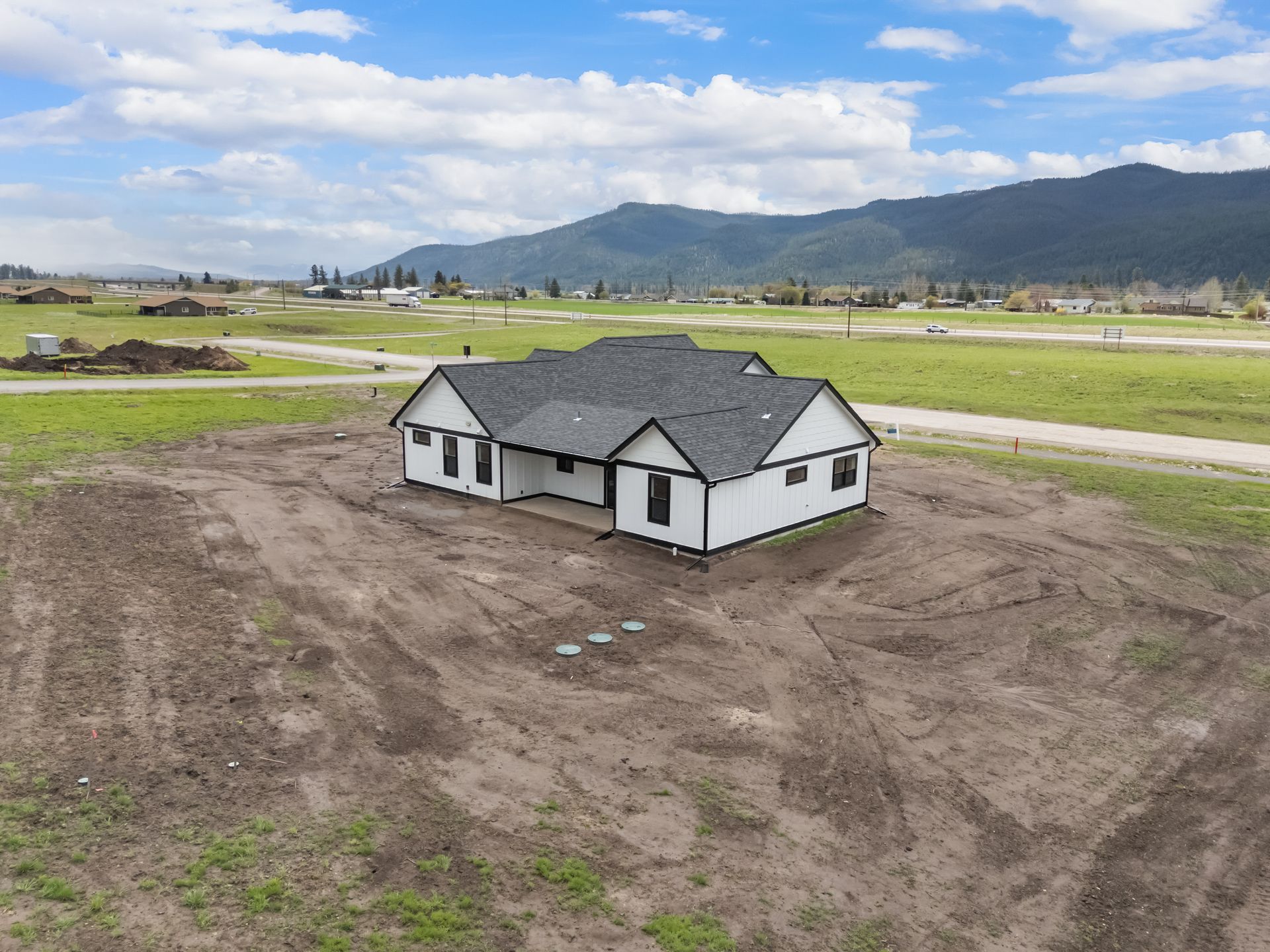 Small white house under construction on a dirt lot with mountains in the background
