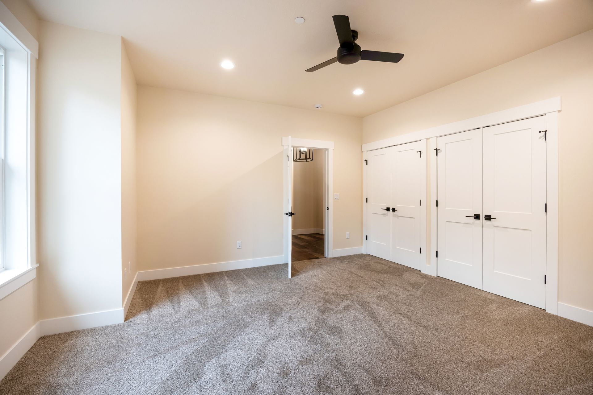 Empty beige bedroom with carpet, ceiling fan, closet doors, and window light