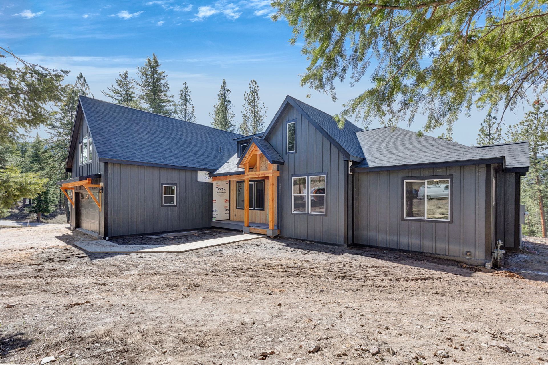 Dark gray modern cabin with orange entry trim, blue roof, and pine trees under a bright sky