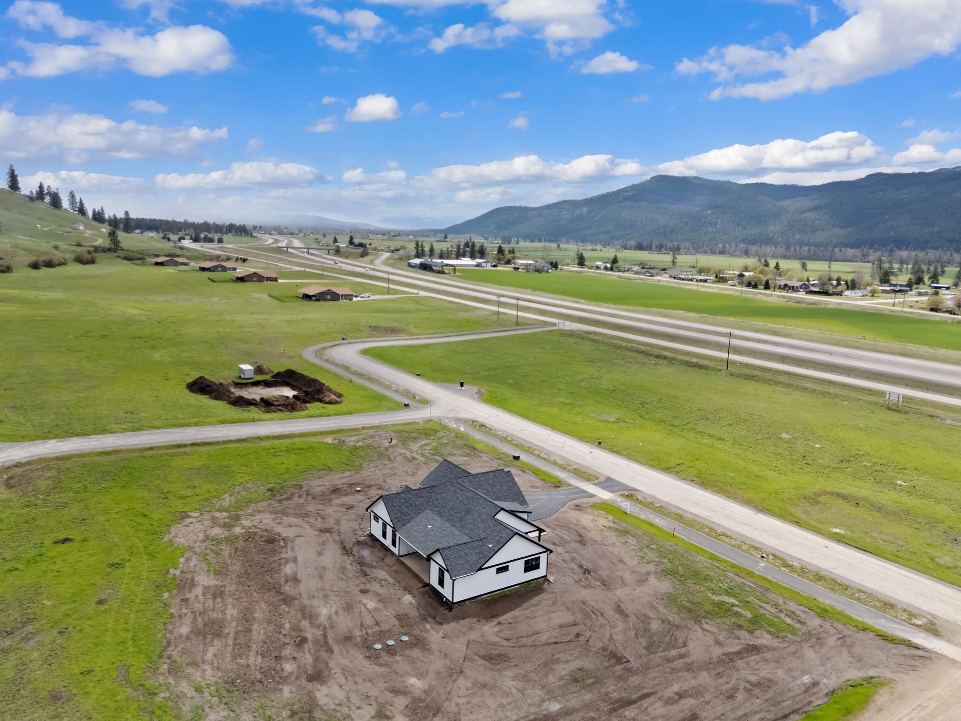 New house under construction in a grassy rural area near a road and runway, with mountains in the background