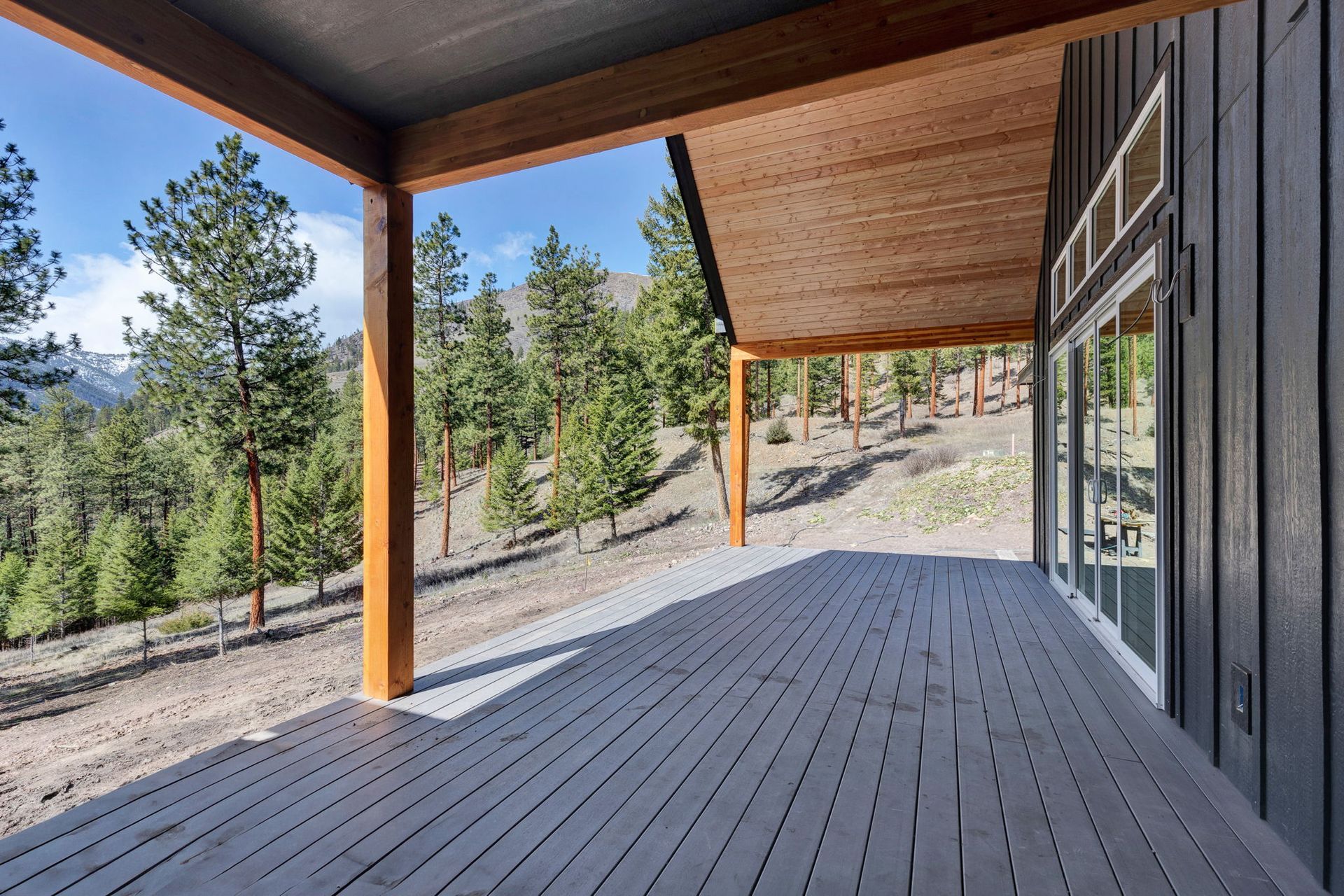 Covered wooden deck with forest and mountain view, featuring timber posts and a sloped hillside.
