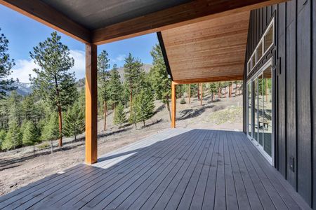 Covered wooden deck overlooking pine trees and a rocky hillside under a bright blue sky