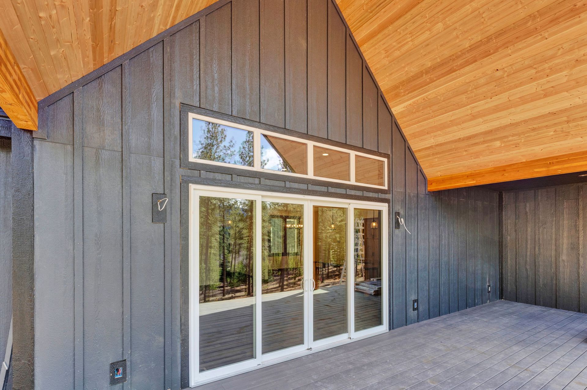 Modern house exterior with gray siding, wood soffits, and sliding glass doors to a deck