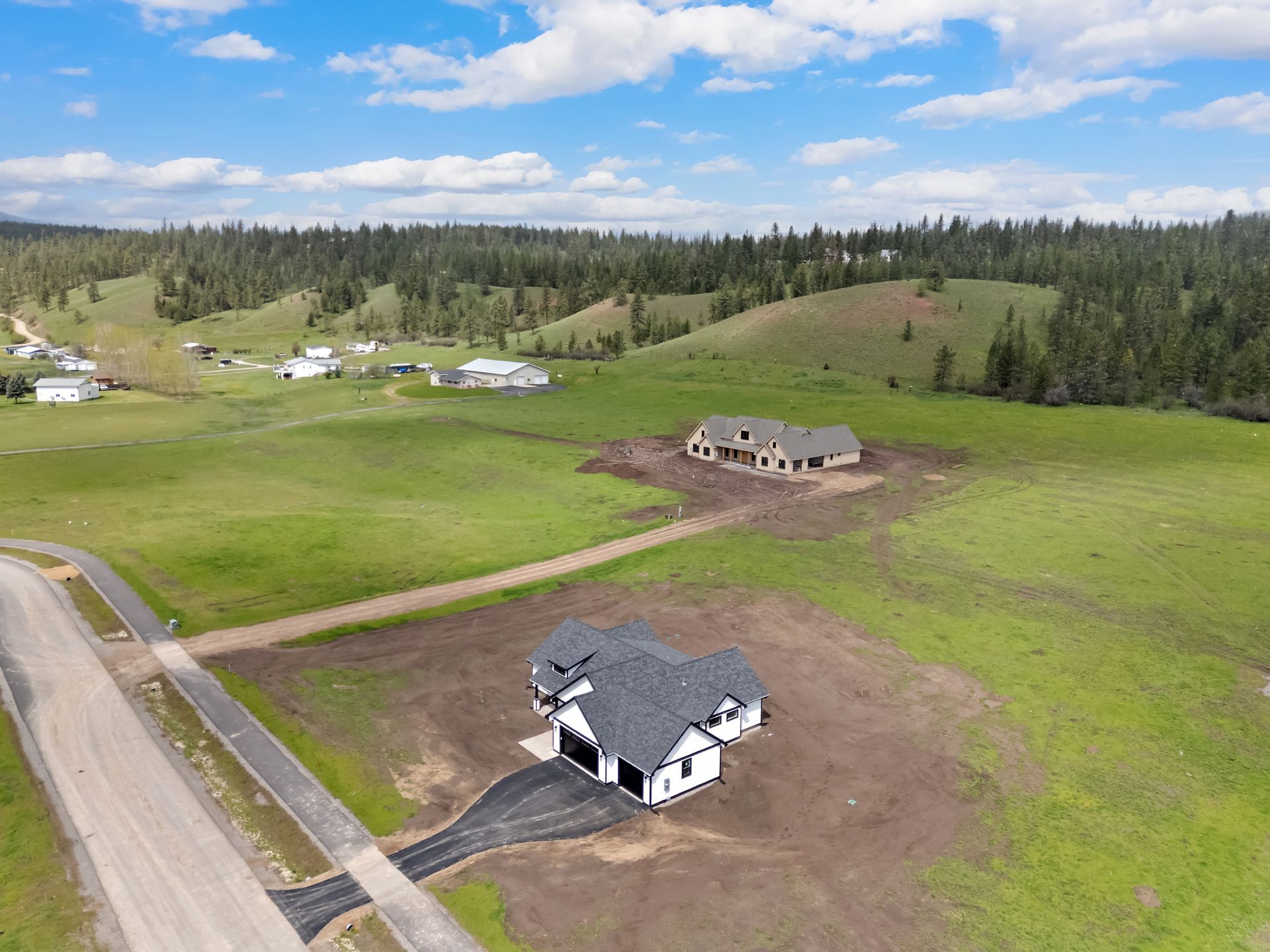 Aerial view of a rural neighborhood with houses, green fields, and a road under a blue sky.