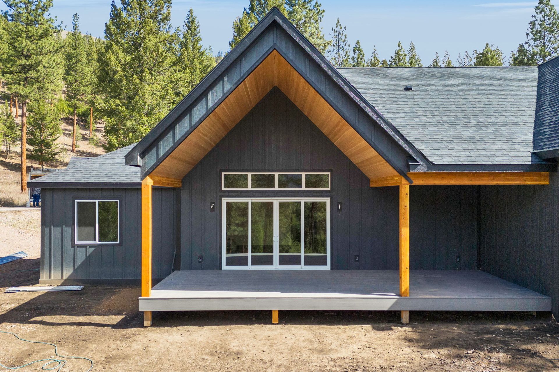 Modern dark-gray house exterior with a covered front porch and pine trees in the background