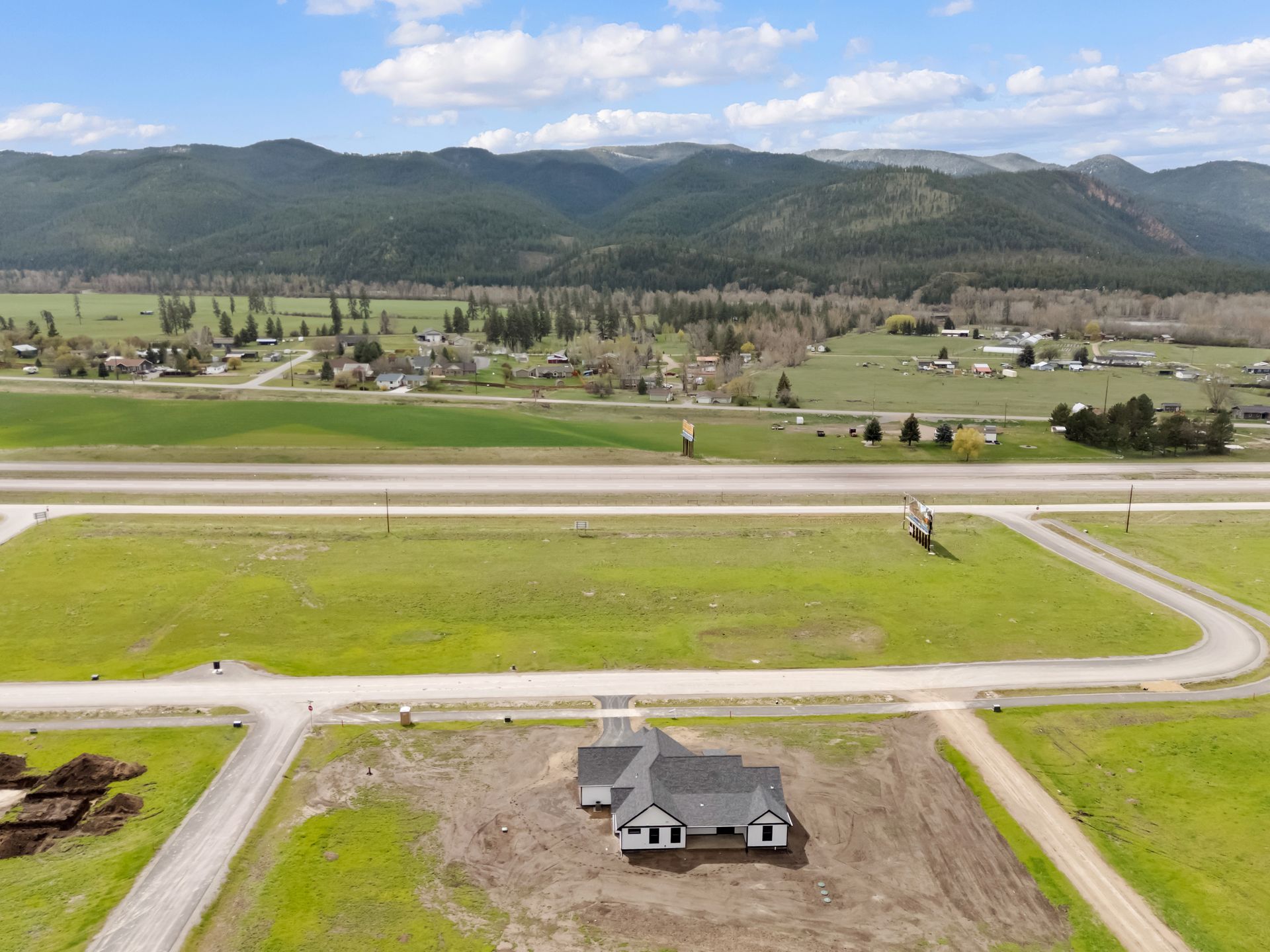 Aerial view of a rural neighborhood with a house, roads, green fields, and mountains in the distance