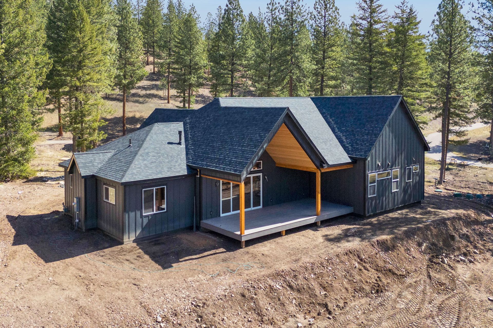Dark gray cabin with covered porch in a pine forest clearing under bright daylight