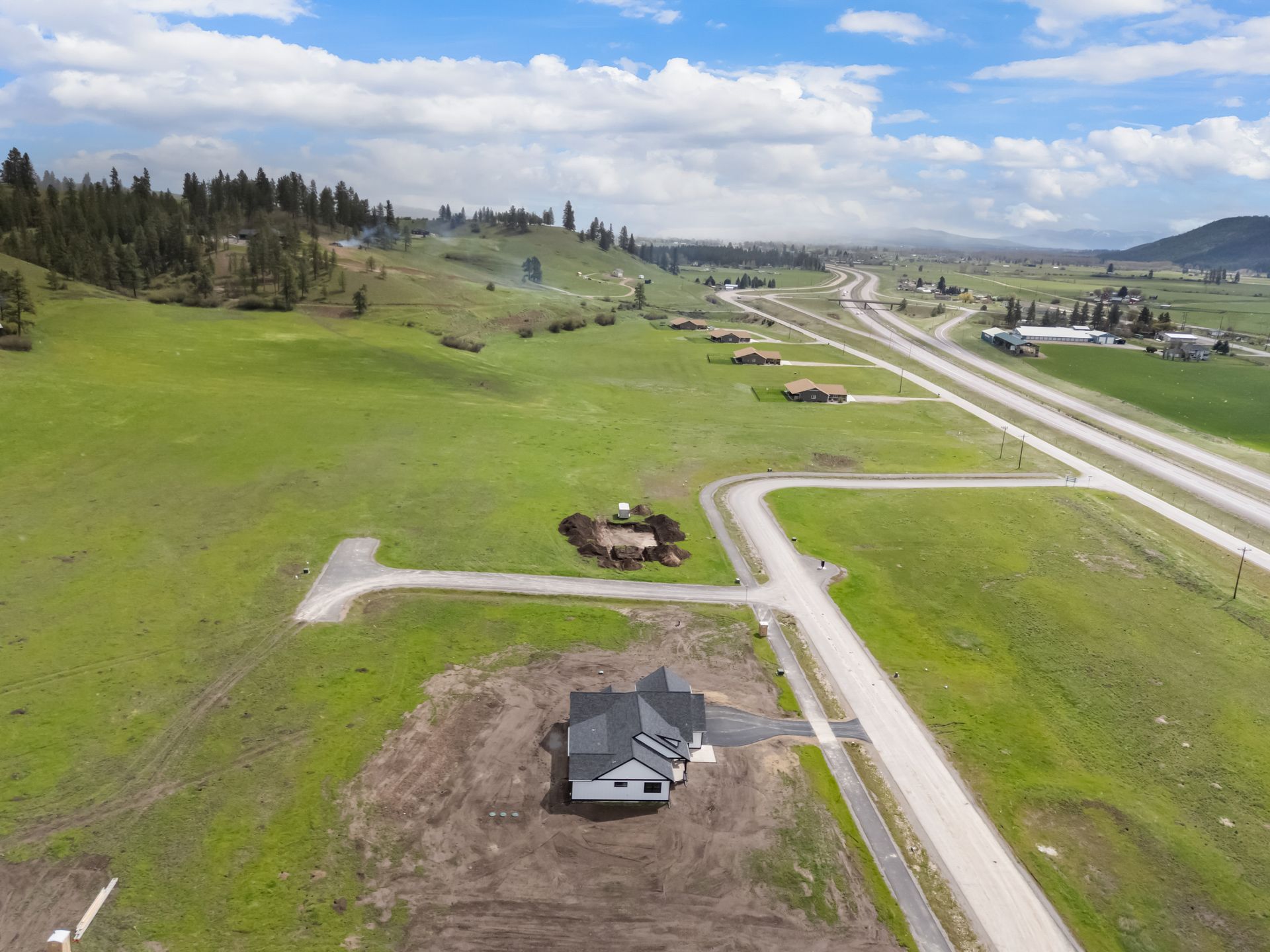 Aerial view of a grassy suburban lot with a house, winding road, and highway under construction nearby