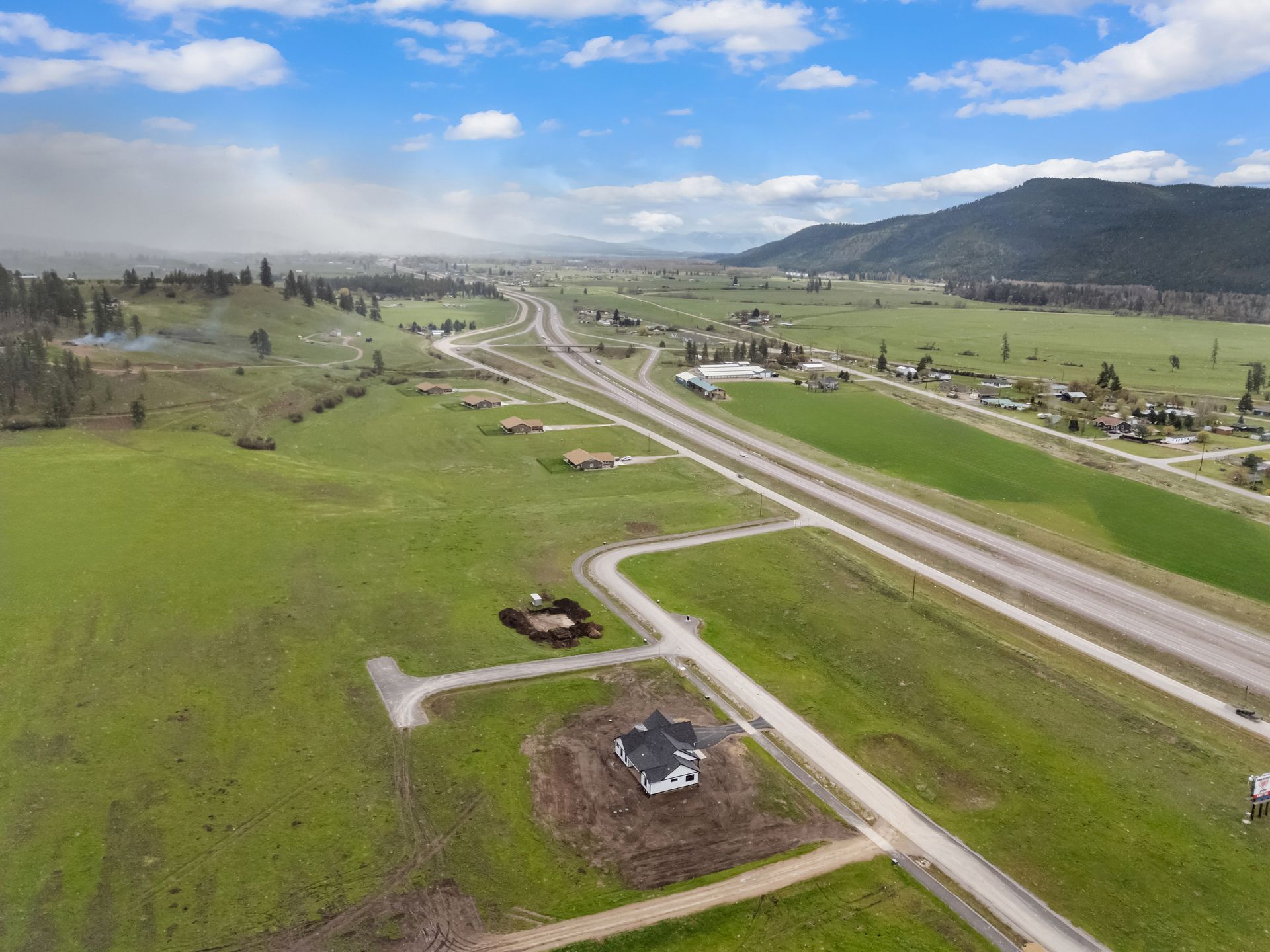 Aerial view of a rural highway cutting through green fields under a cloudy sky.
