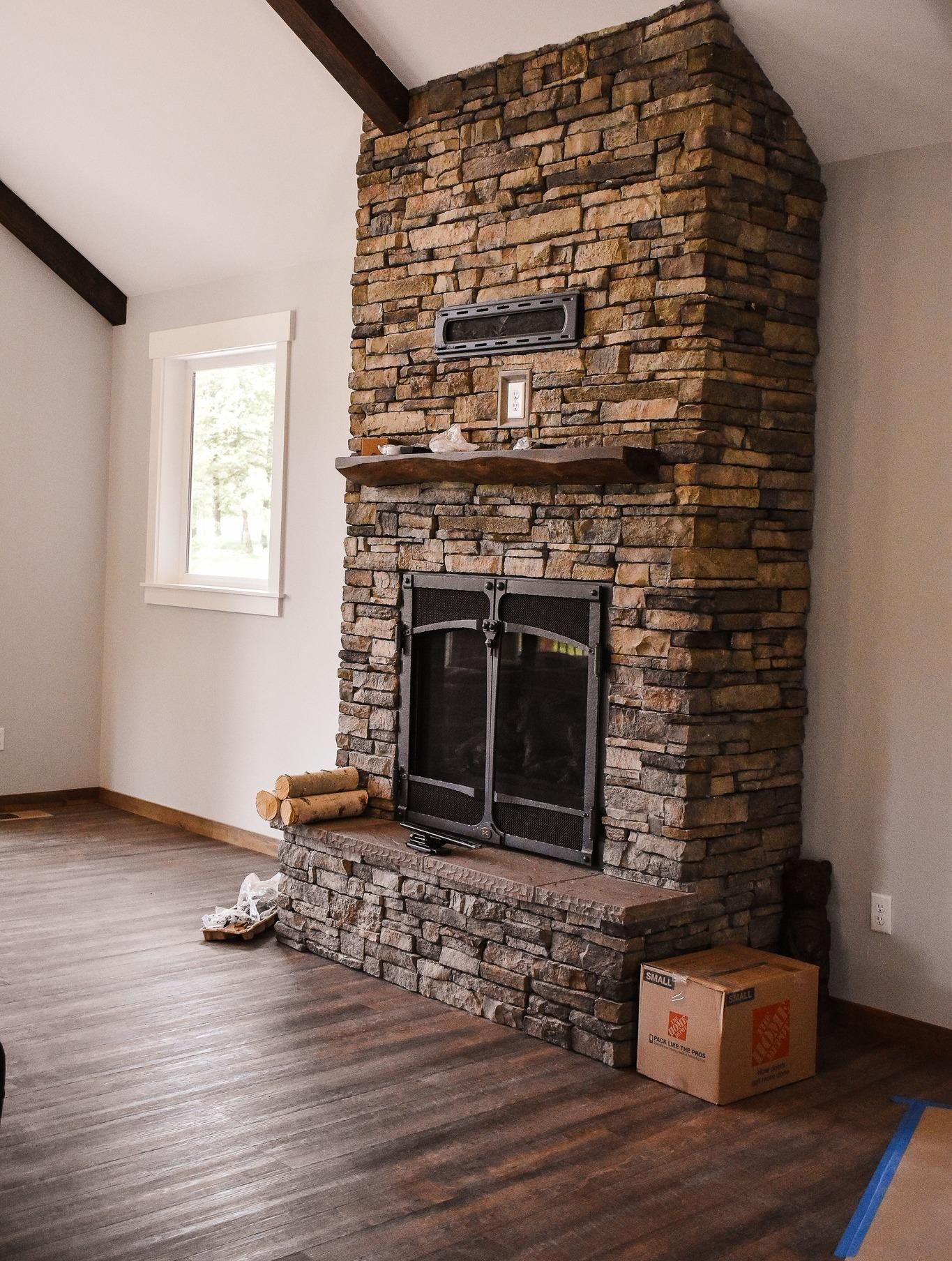 Stone fireplace in a room with hardwood floors and a window; moving boxes sit nearby.
