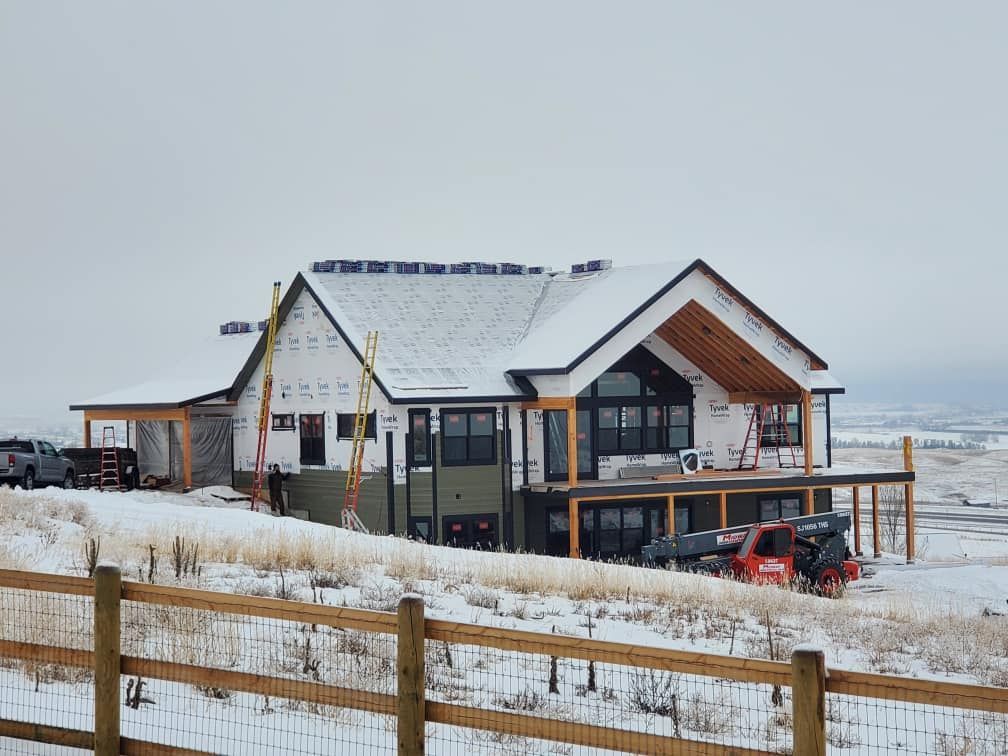 Modern house under construction in a snowy field with a wooden fence and excavator nearby