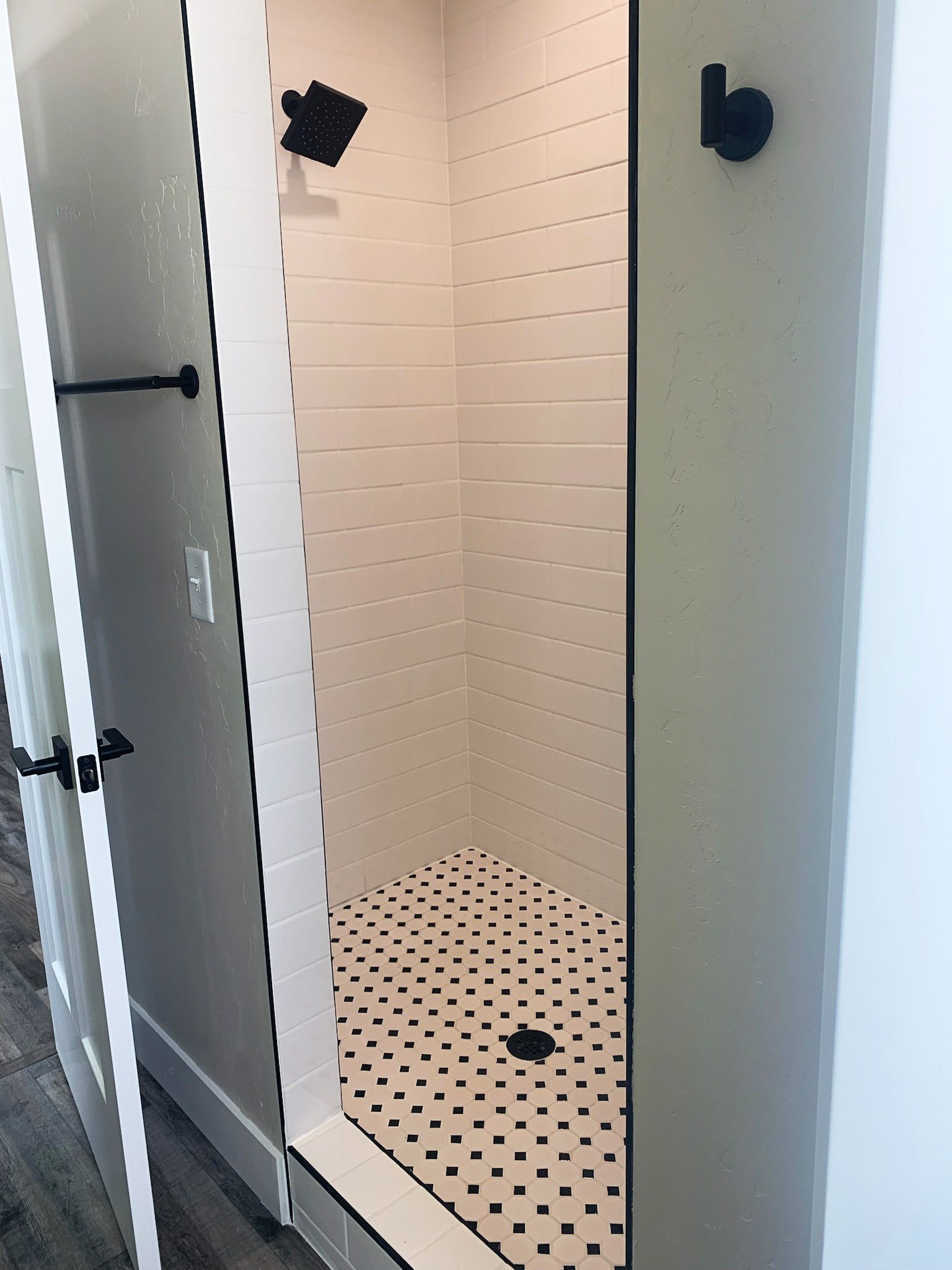 Small tiled shower stall with black hex floor tiles and a mounted showerhead.