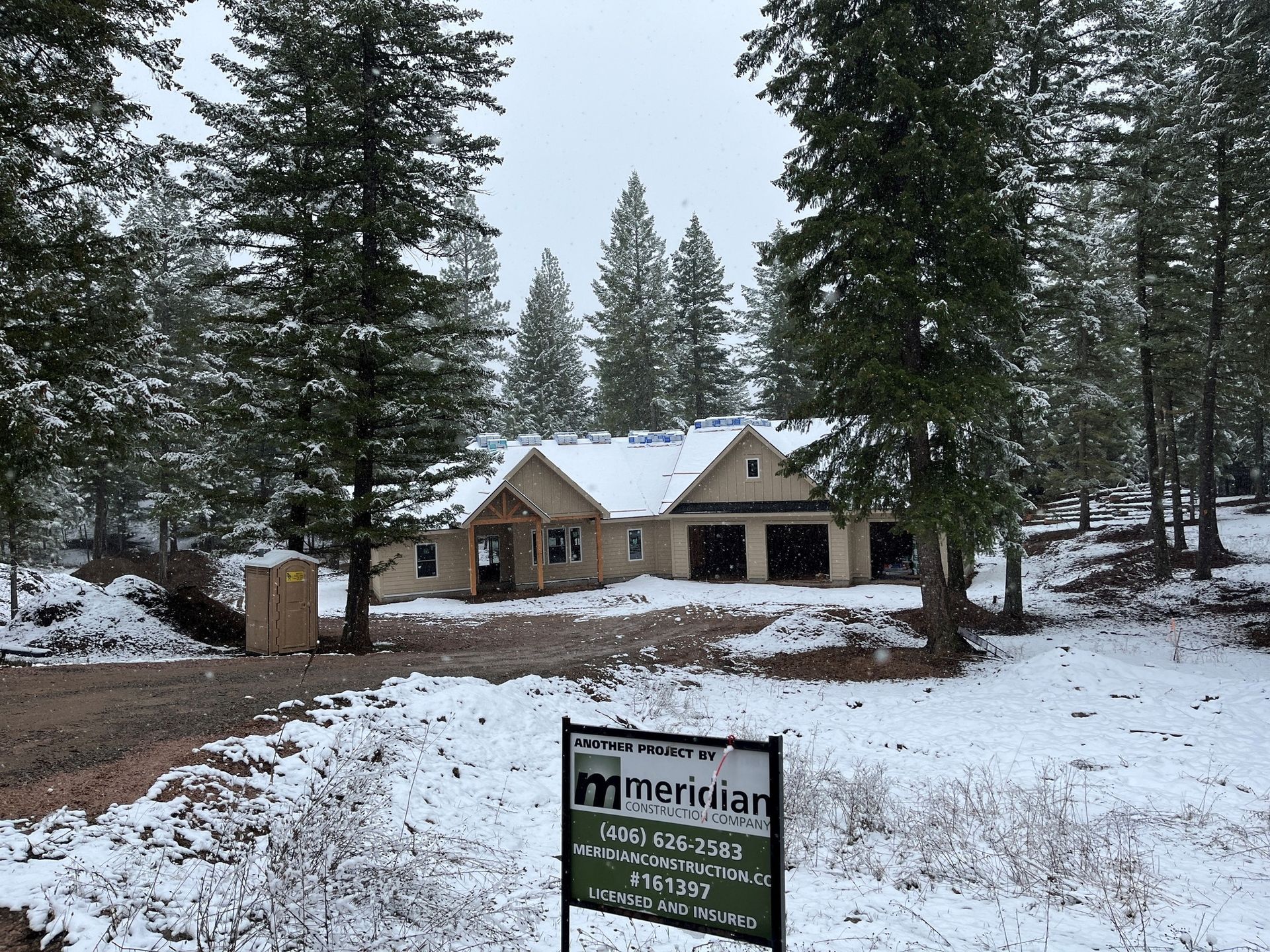 Snowy cabin under tall pine trees with a Meridian sign in the foreground
