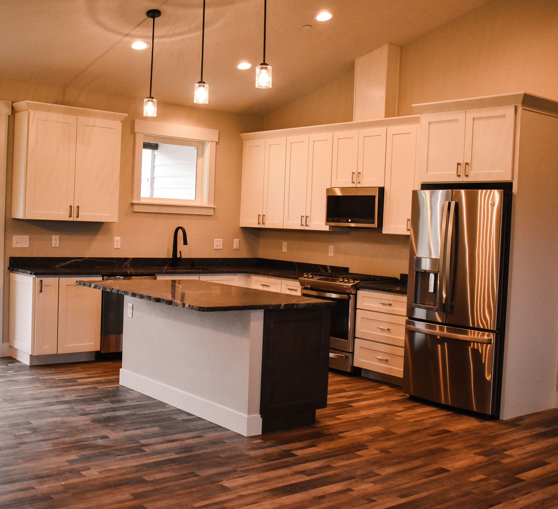 Modern kitchen with white cabinets, stainless steel appliances, an island, and wood flooring.