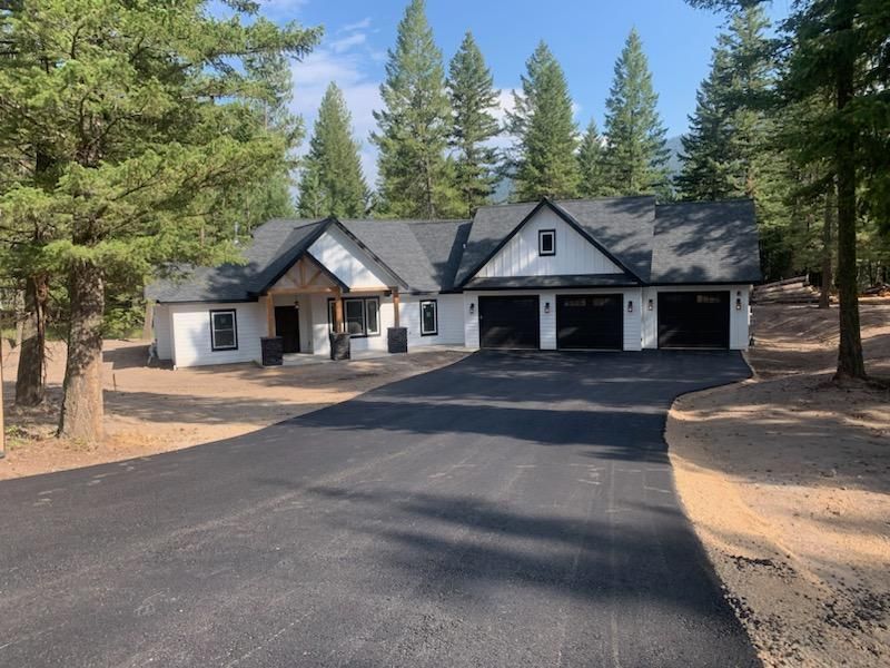 Large house with dark roof and three-car garage, set among pine trees with a paved driveway
