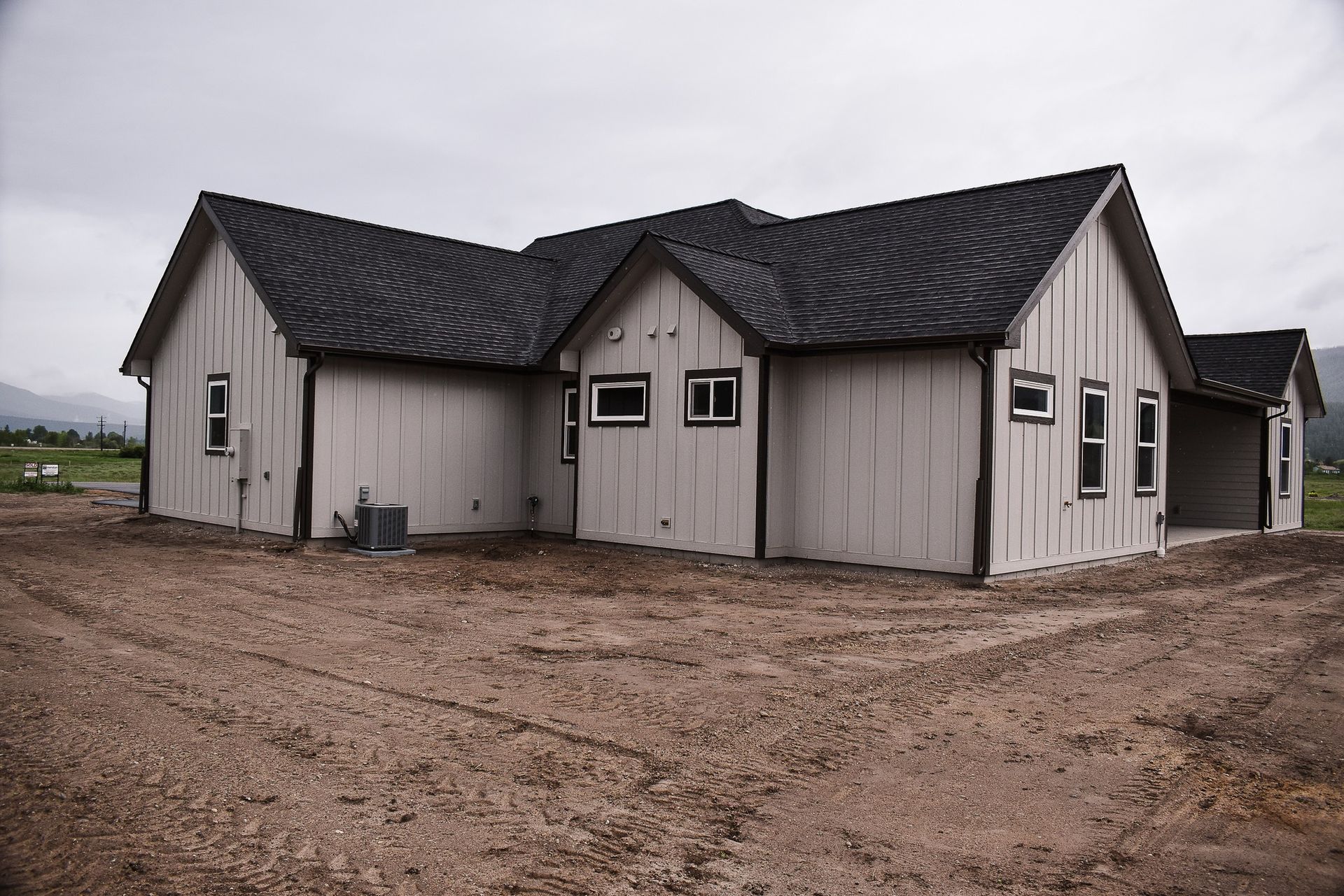 Small beige house with a dark roof on a muddy, overcast lot