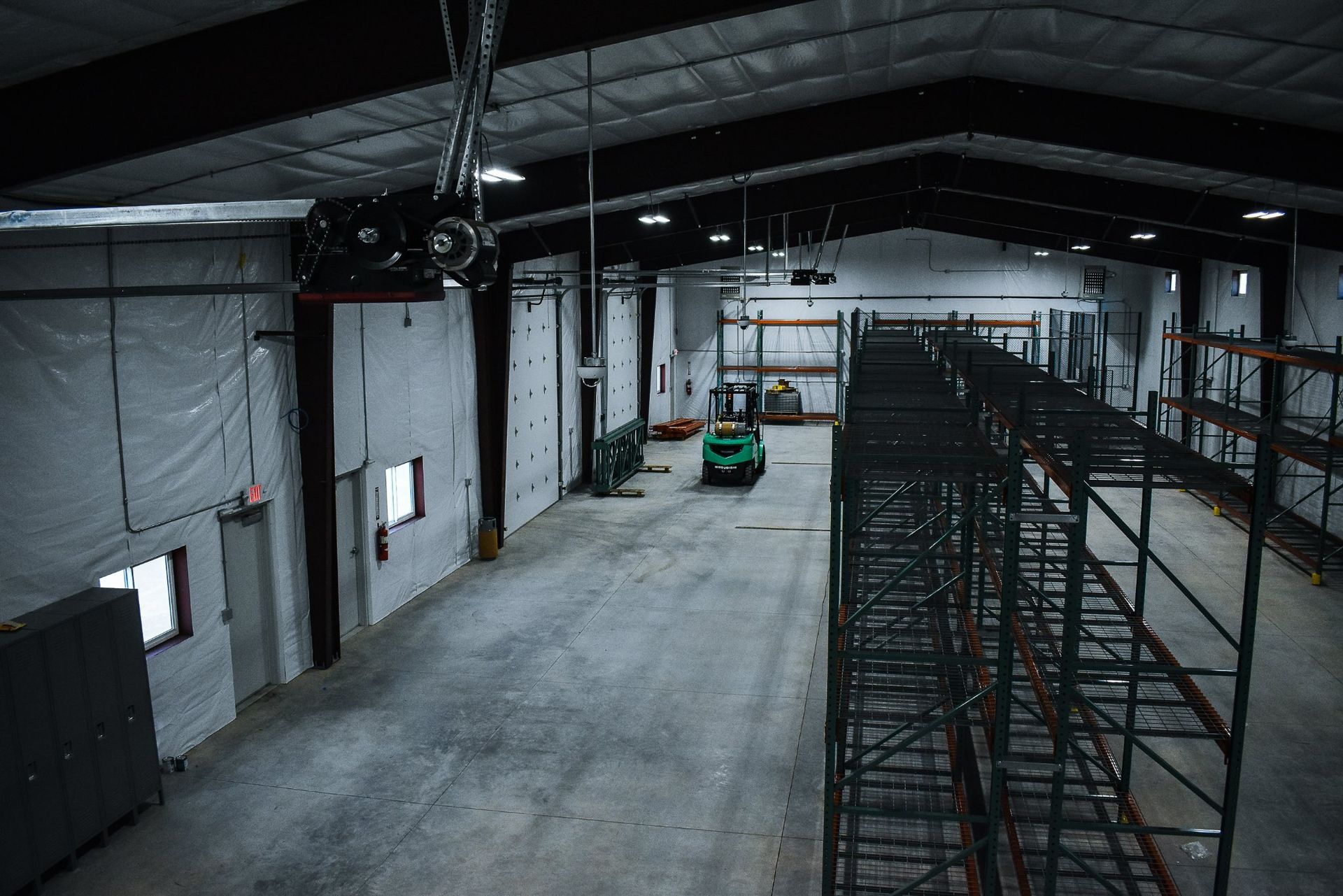 Empty warehouse interior with scaffolding and a small green vehicle on a concrete floor