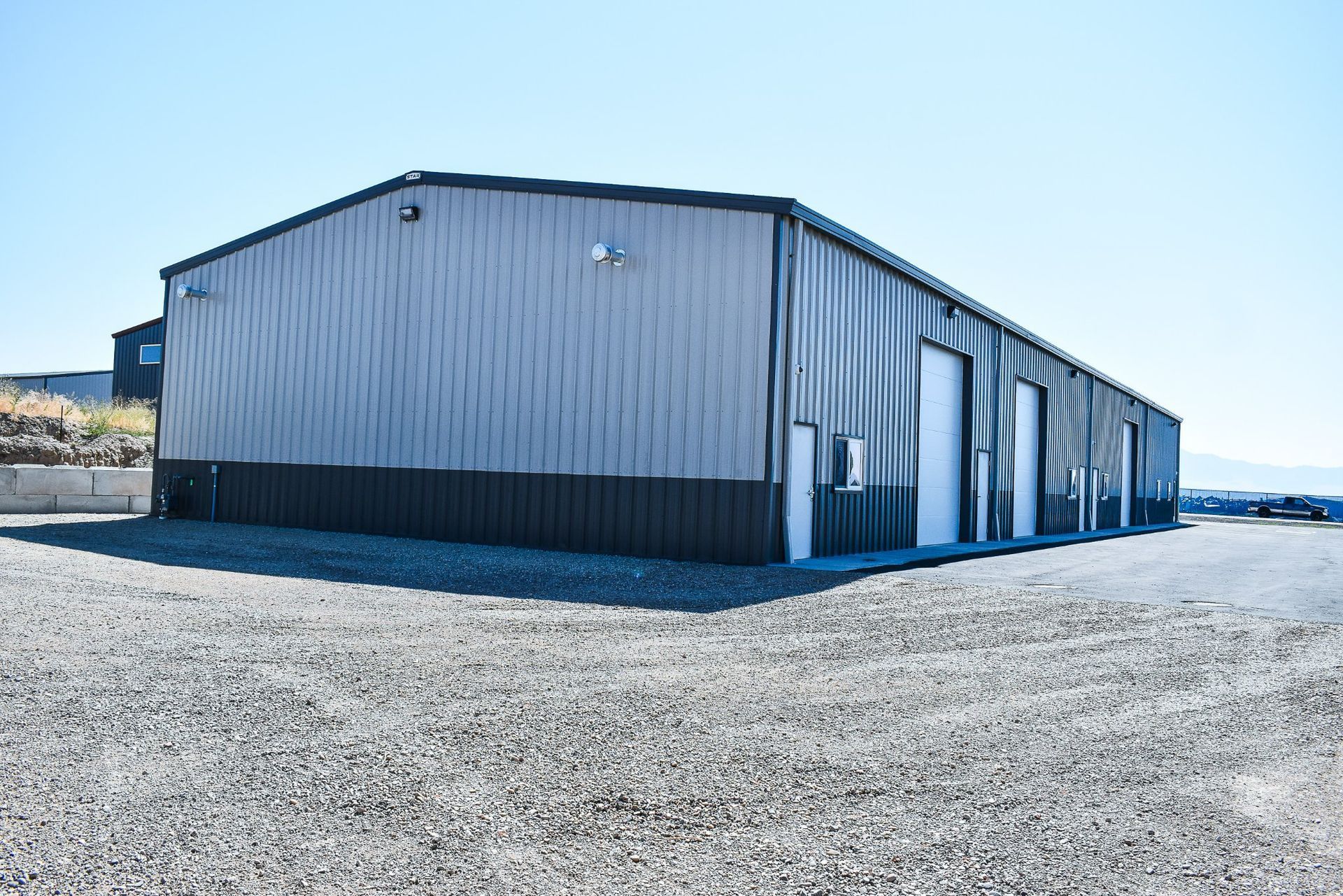 Long gray metal warehouse on a gravel lot under a clear blue sky