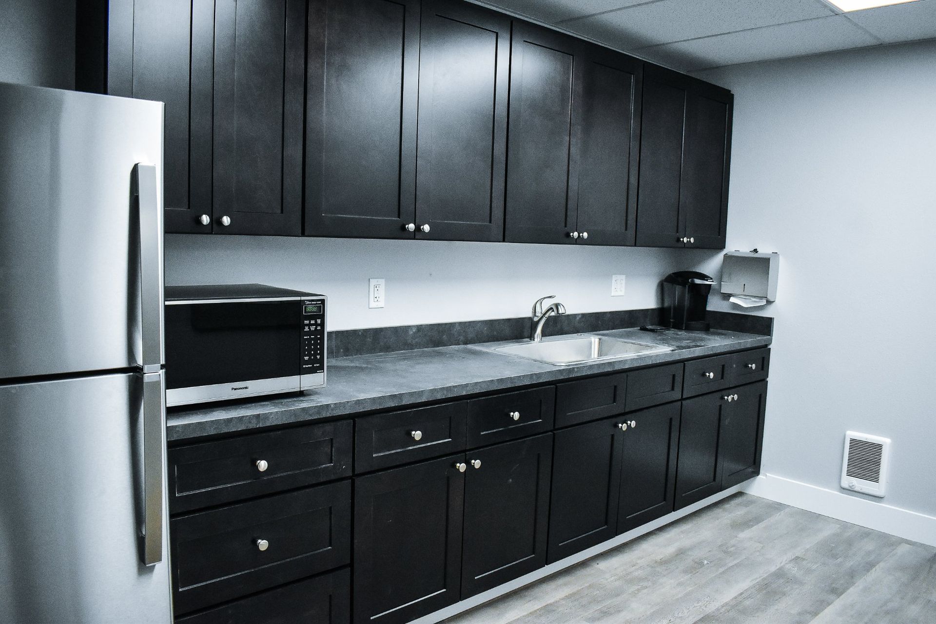 Modern kitchen with dark cabinets, stainless steel fridge, speckled countertop, and small appliances