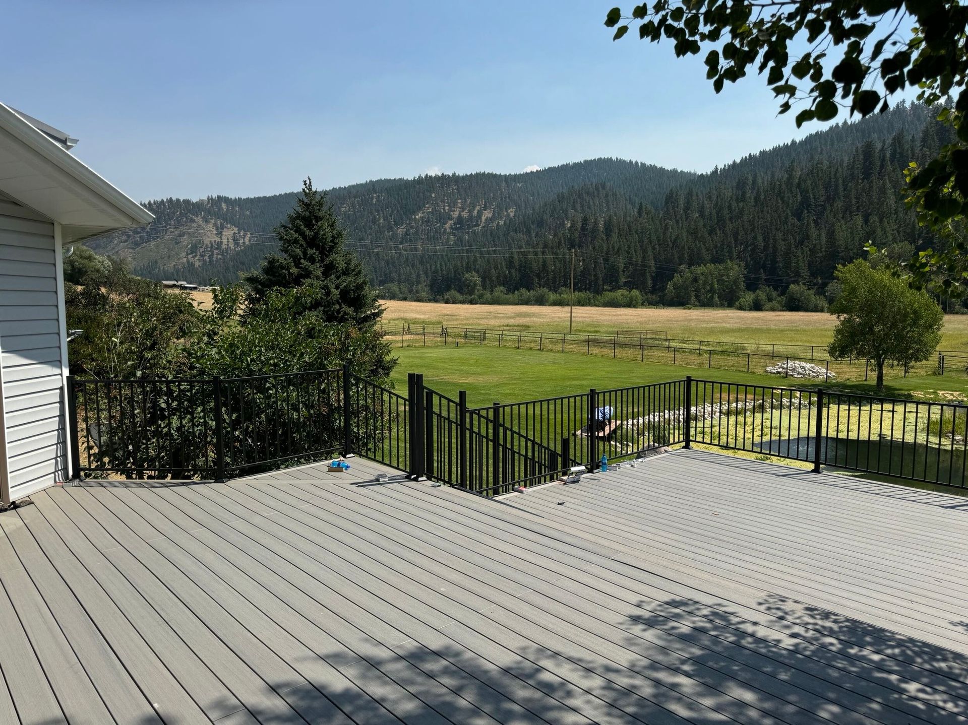 Wooden deck overlooking a fenced yard, trees, and distant forested hills on a sunny day