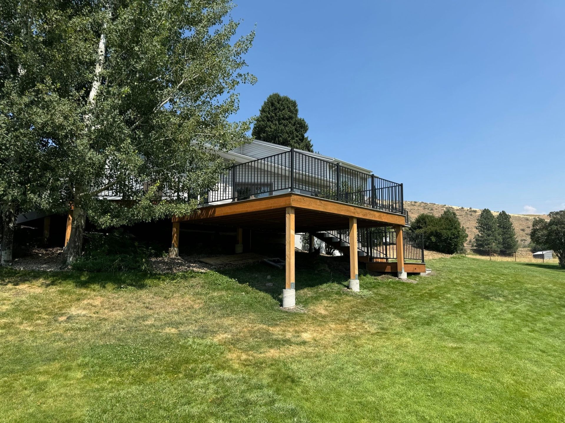 Raised deck with glass railing beside a grassy lawn and trees on a sunny day