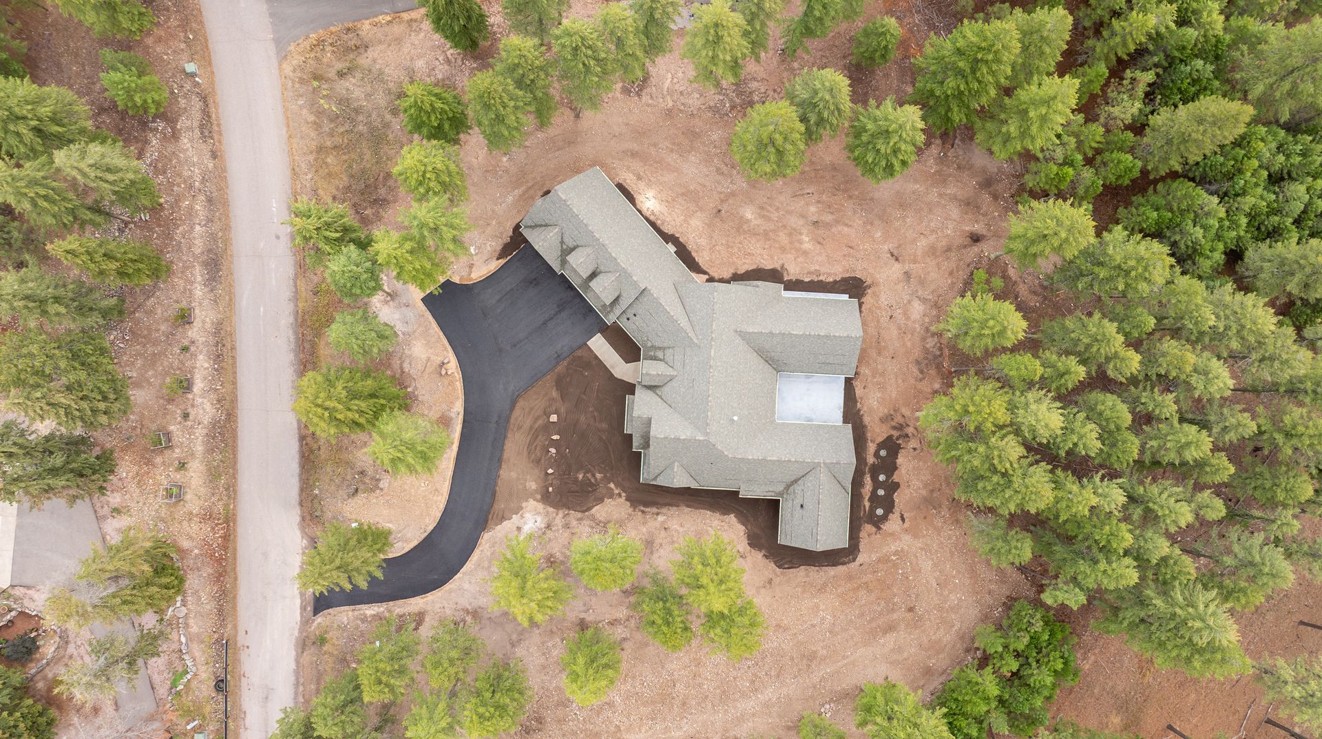 Aerial view of a gray house with a curved driveway, surrounded by trees and brown ground.