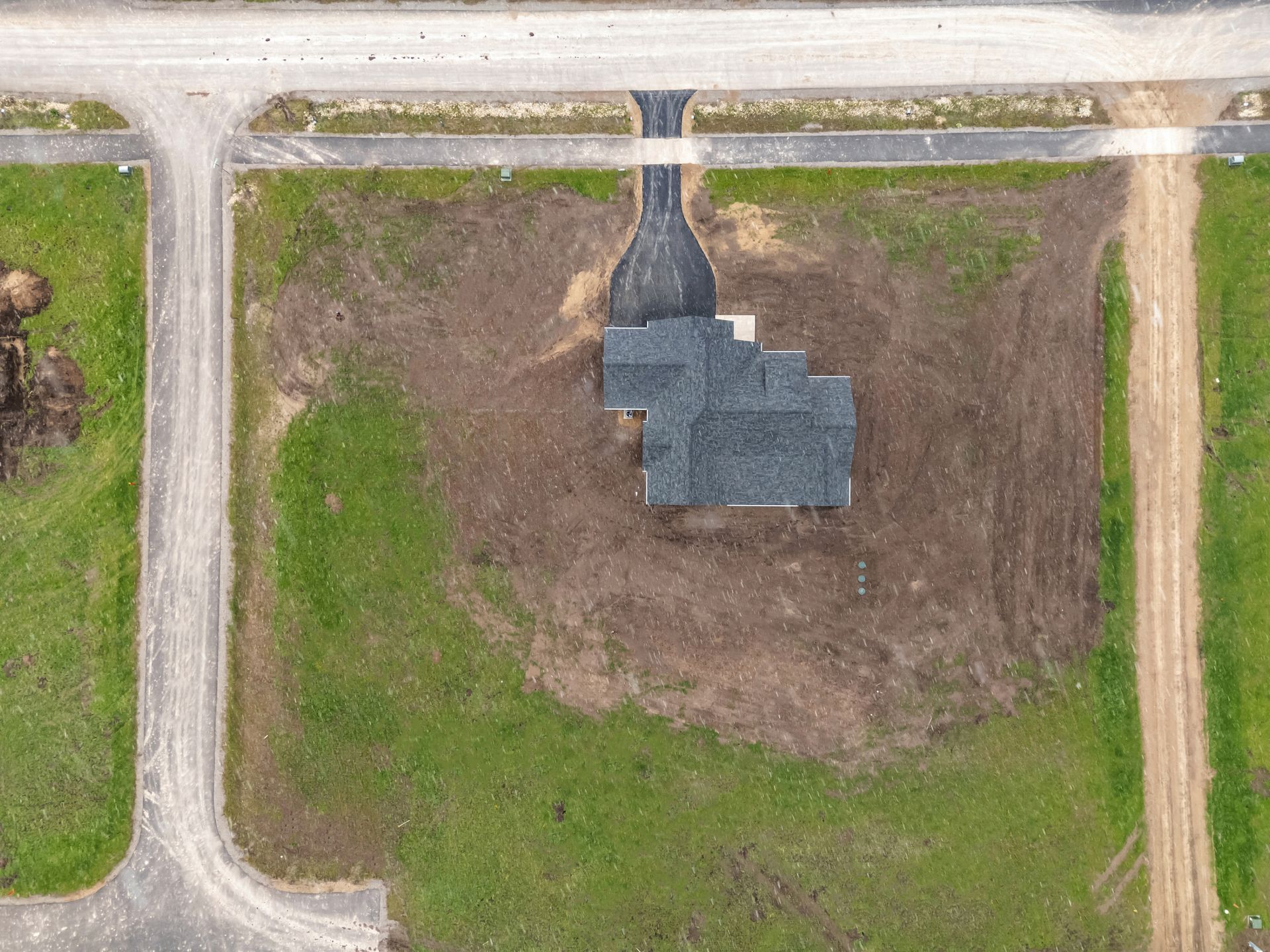Aerial view of a house under construction beside roads and grassy land.