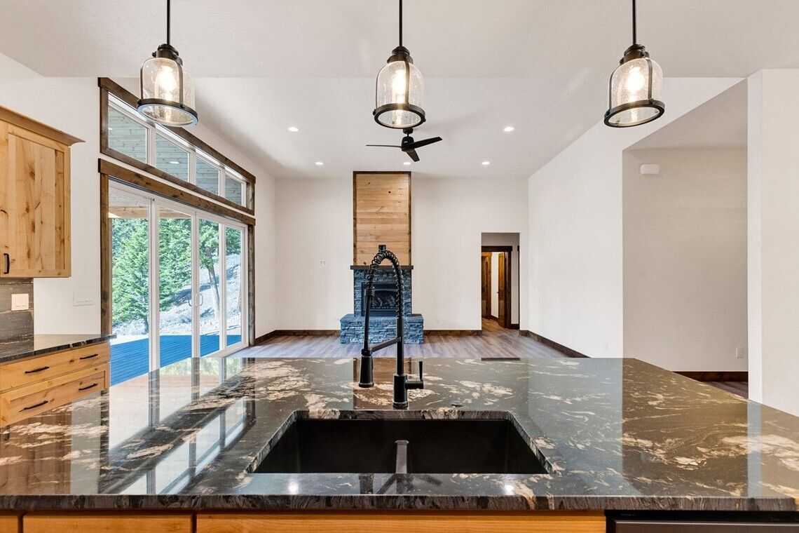 Modern open-concept kitchen with black countertops, pendant lights, and large sliding glass doors overlooking a pool.