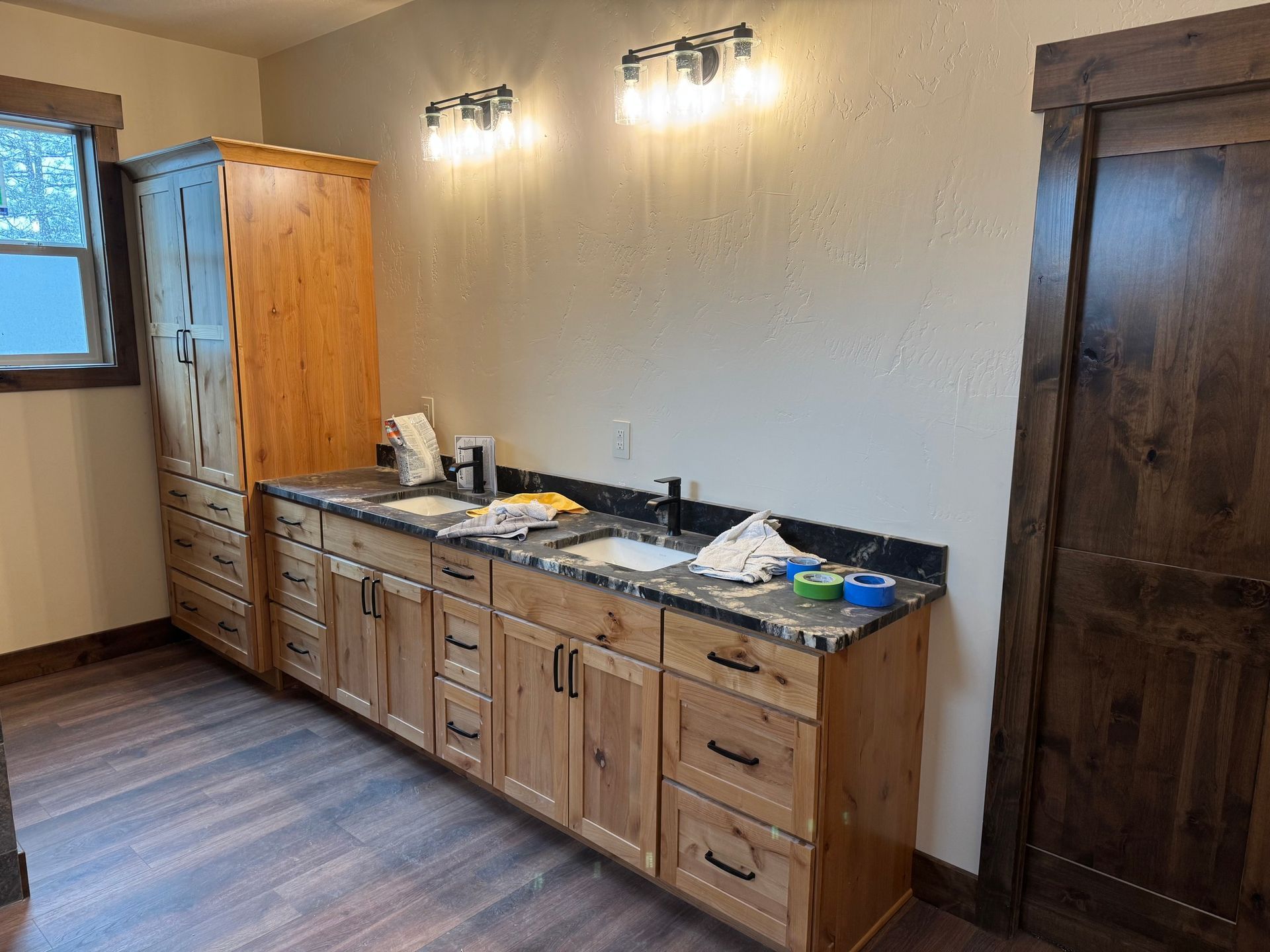 Bathroom vanity with wood cabinets, granite countertop, mirror, and lights against a beige wall