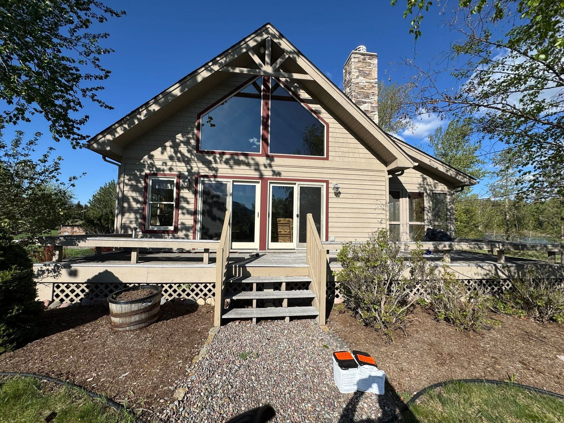 Modern beige house with steep roof, front steps, and a gravel yard under a clear blue sky