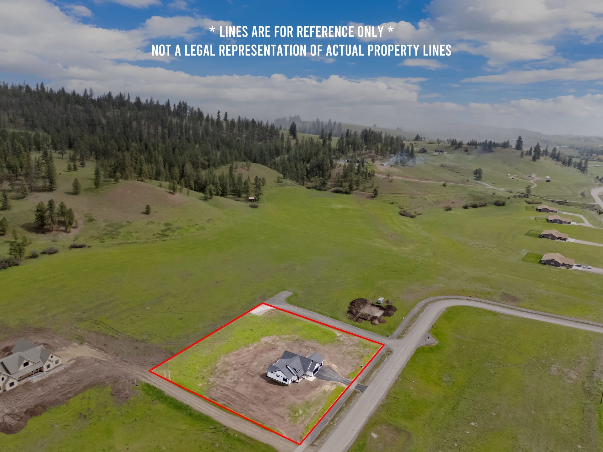 Aerial view of a rural lot outlined in red with a small house pad, surrounded by green fields and trees.
