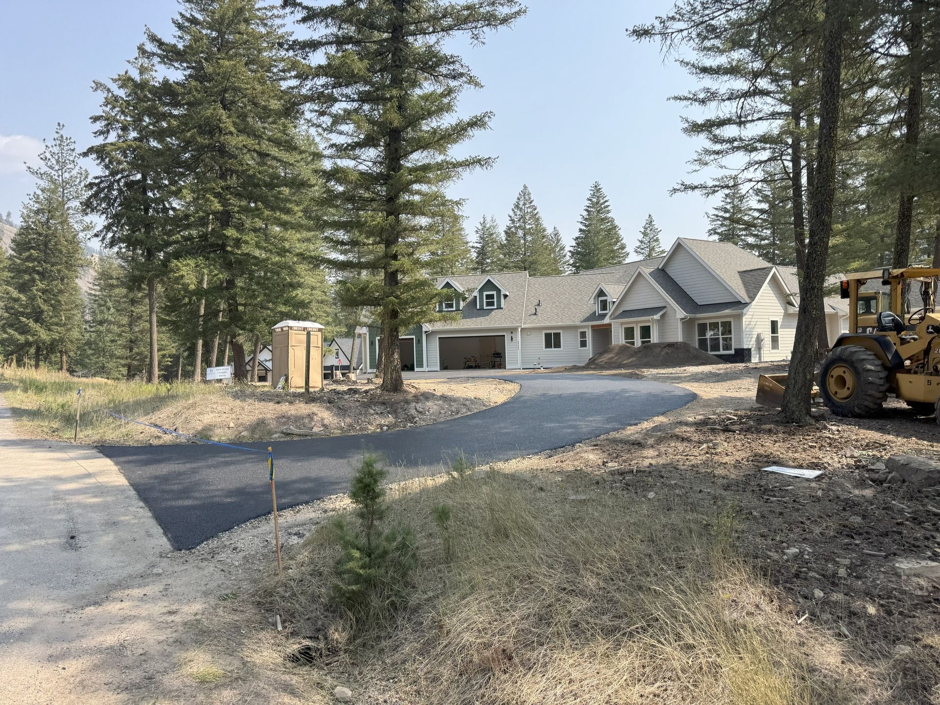 Large house in a wooded rural lot with a gravel driveway and construction equipment nearby