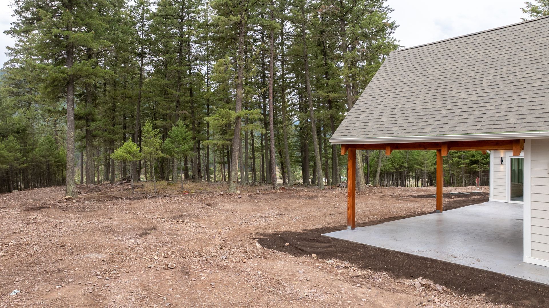 Wooded campsite beside a gray-roofed pavilion with orange posts and gravel ground
