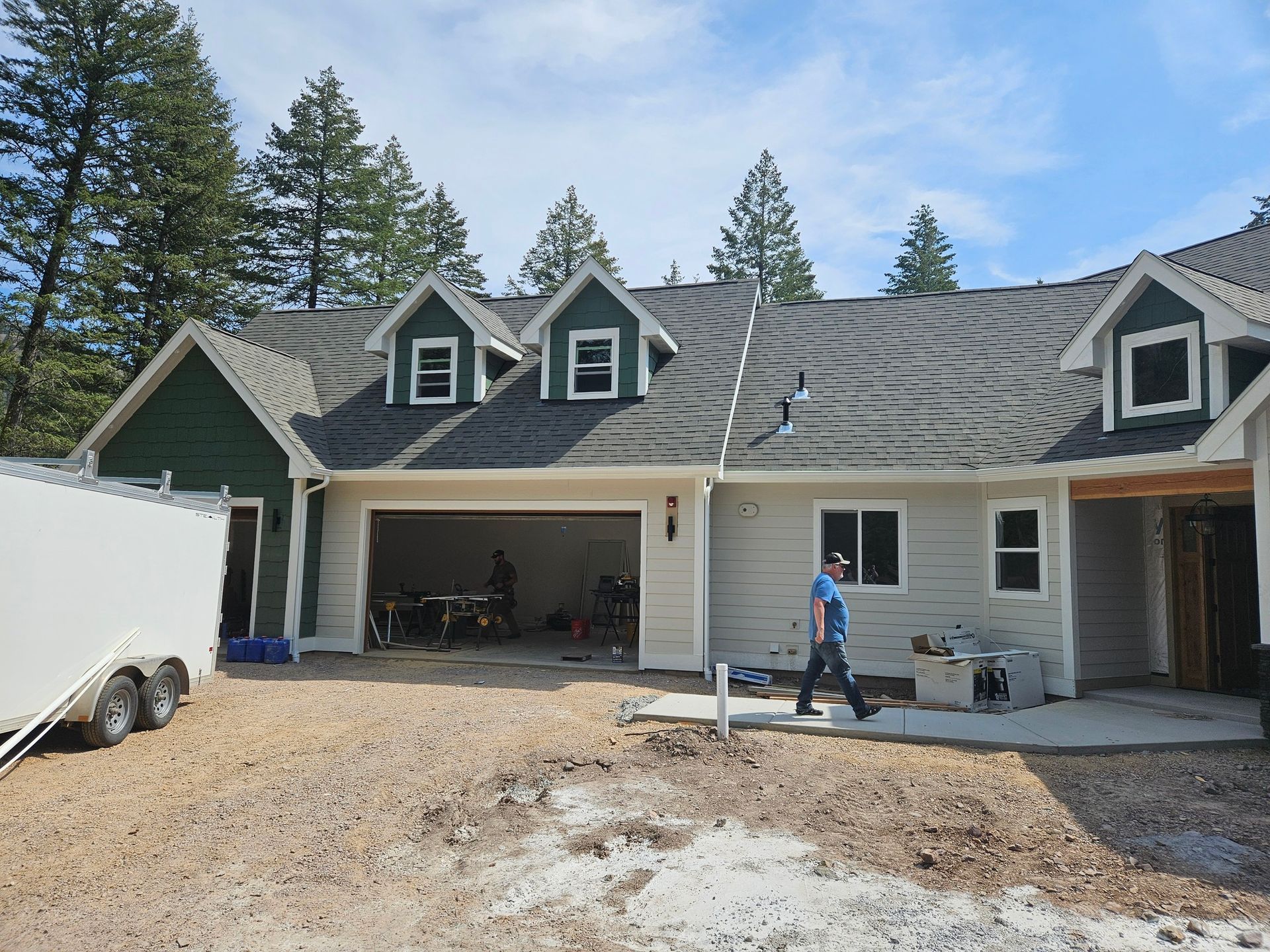 House exterior under renovation with a person working in front of an open garage and gravel driveway