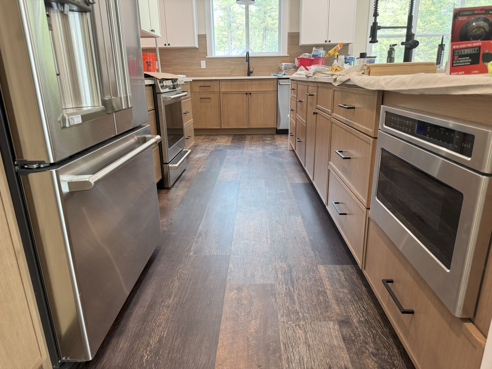 Modern kitchen with stainless steel appliances, wooden cabinets, and a long dark floor leading to a window.