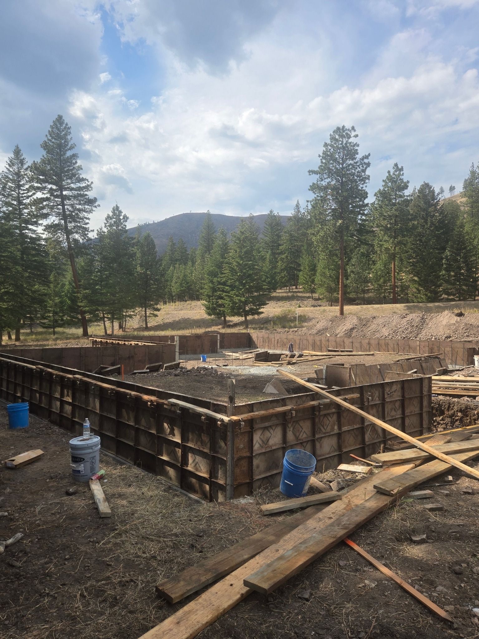 Concrete foundation forms at a wooded construction site with mountains in the background
