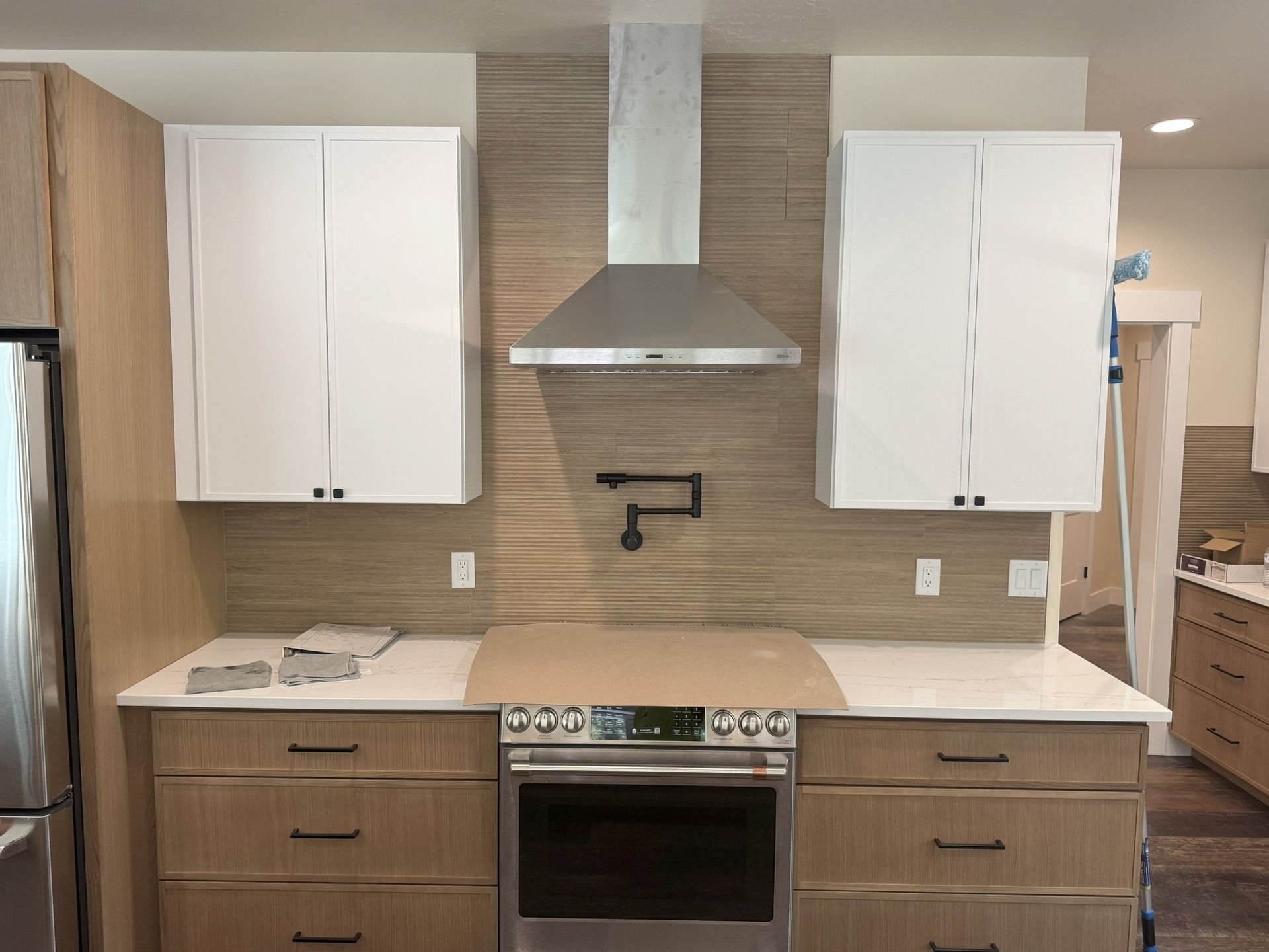 Modern kitchen with white cabinets, stainless steel range hood, oven, and beige countertops.