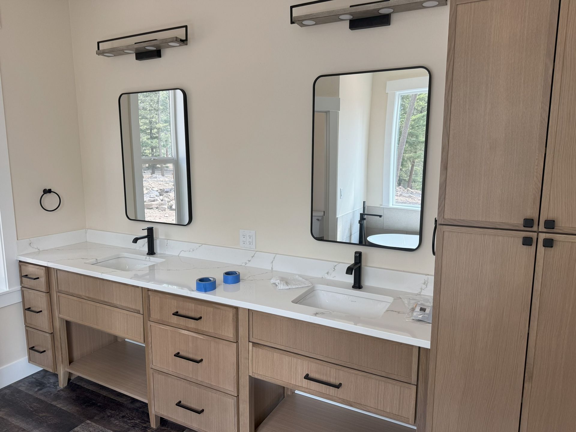 Modern bathroom vanity with two mirrors, black faucets, wood cabinets, and daylight from windows