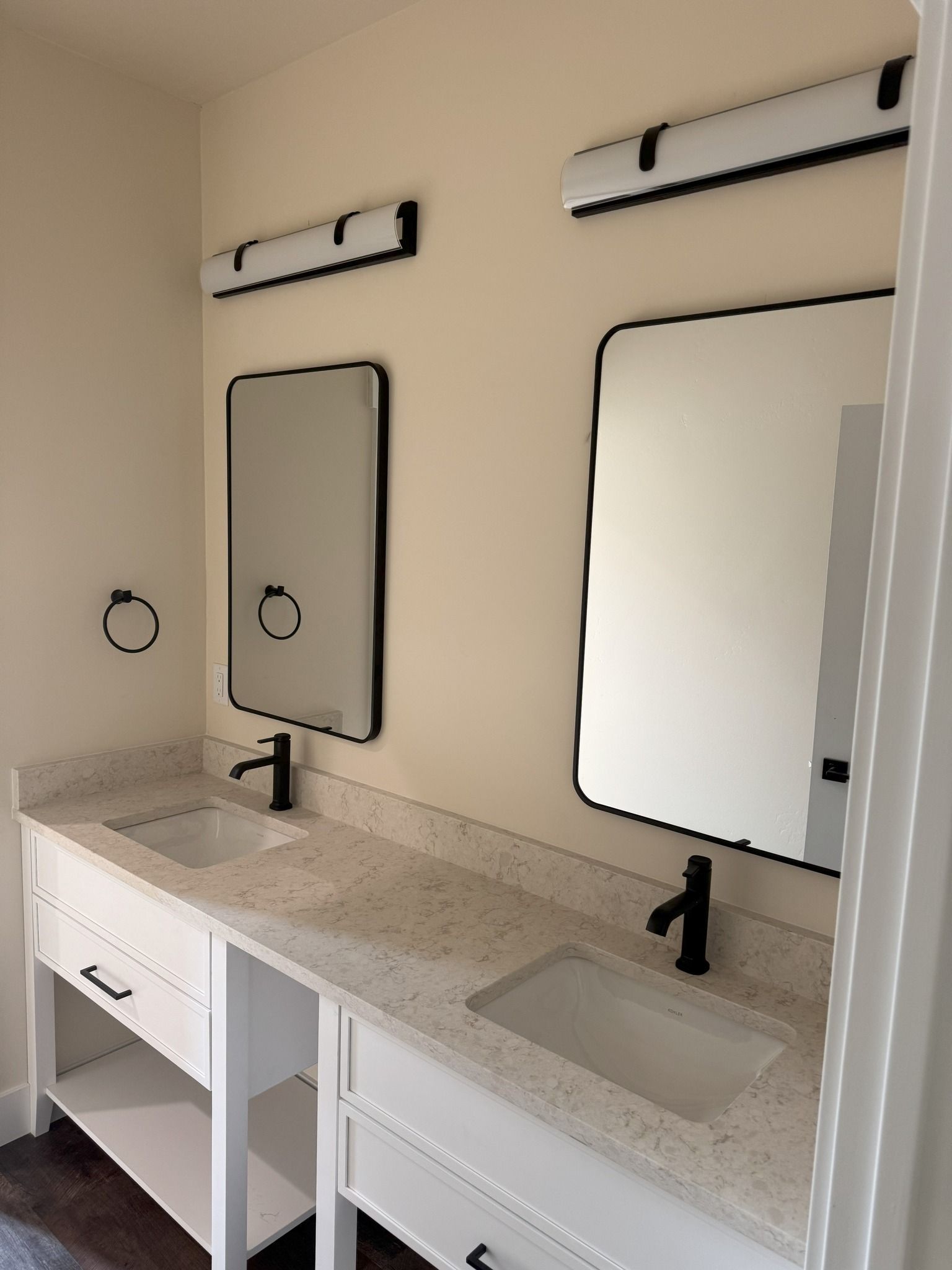 Modern bathroom vanity with double sinks, two mirrors, and wall-mounted lights in a beige room