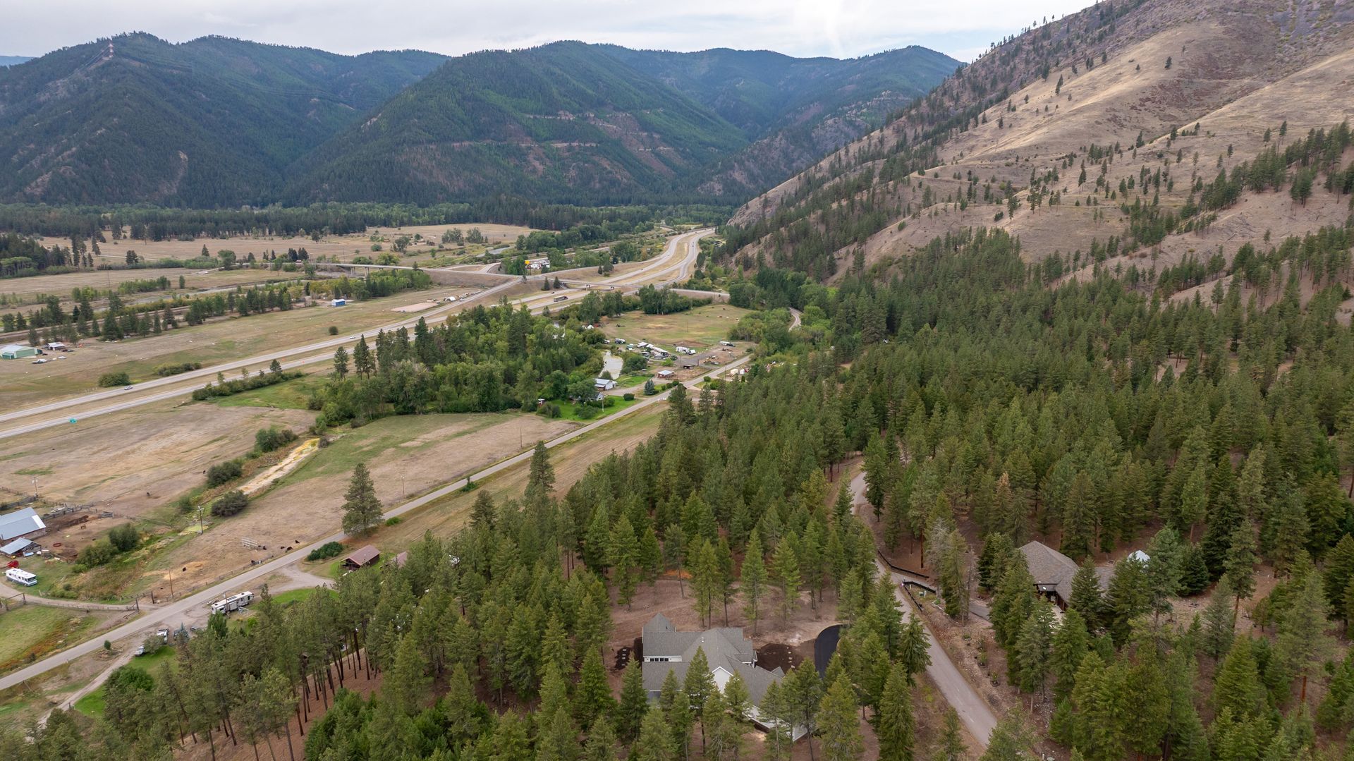 Wide aerial view of a green valley with forested hills, a riverbed, and mountains in the distance
