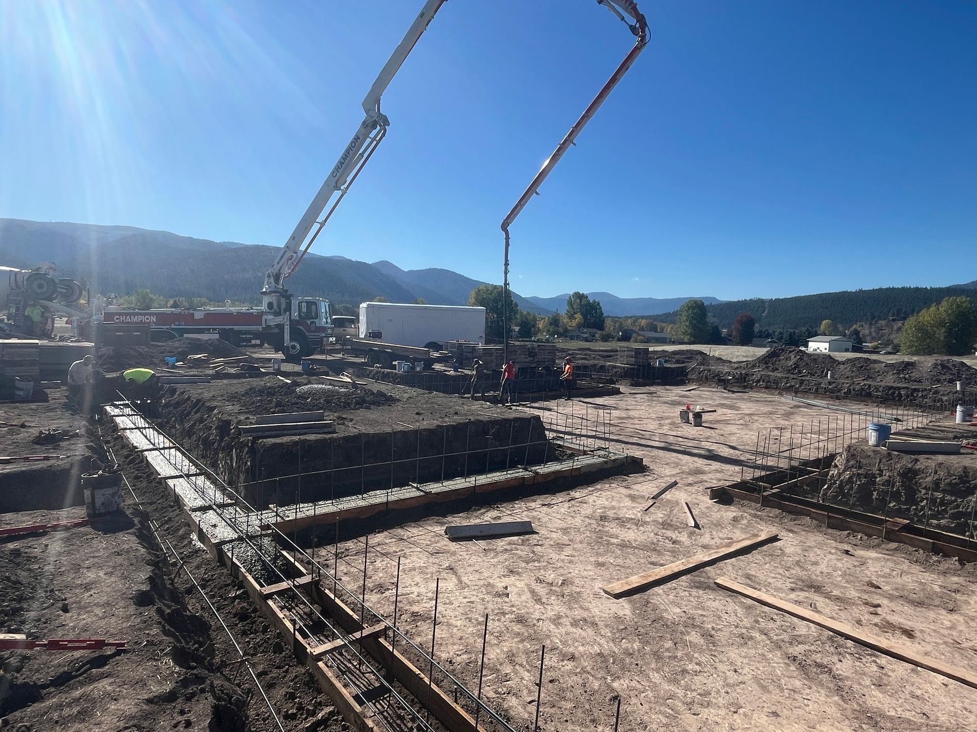 Concrete foundation construction site with pump truck arms and workers under a clear blue sky