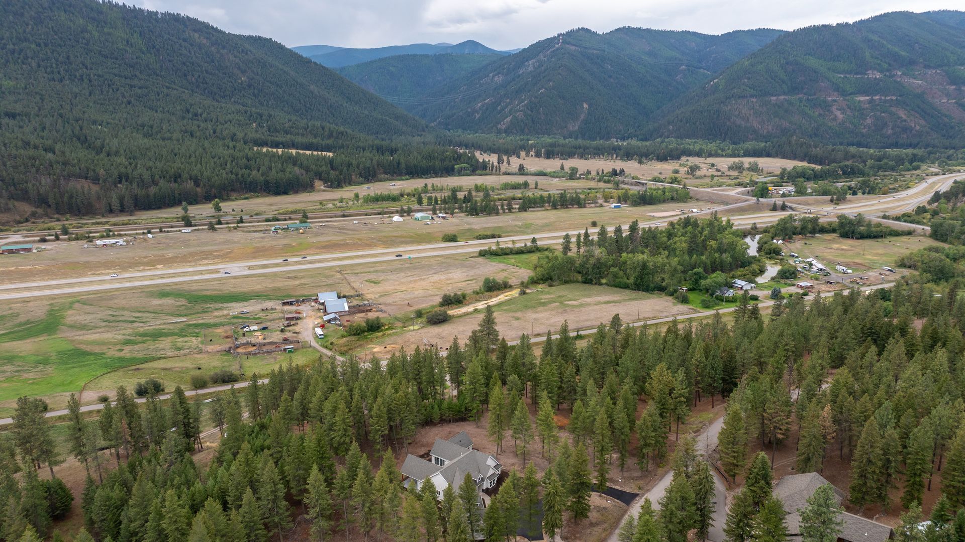 Mountain valley with scattered fields, forested slopes, and a small town under cloudy skies