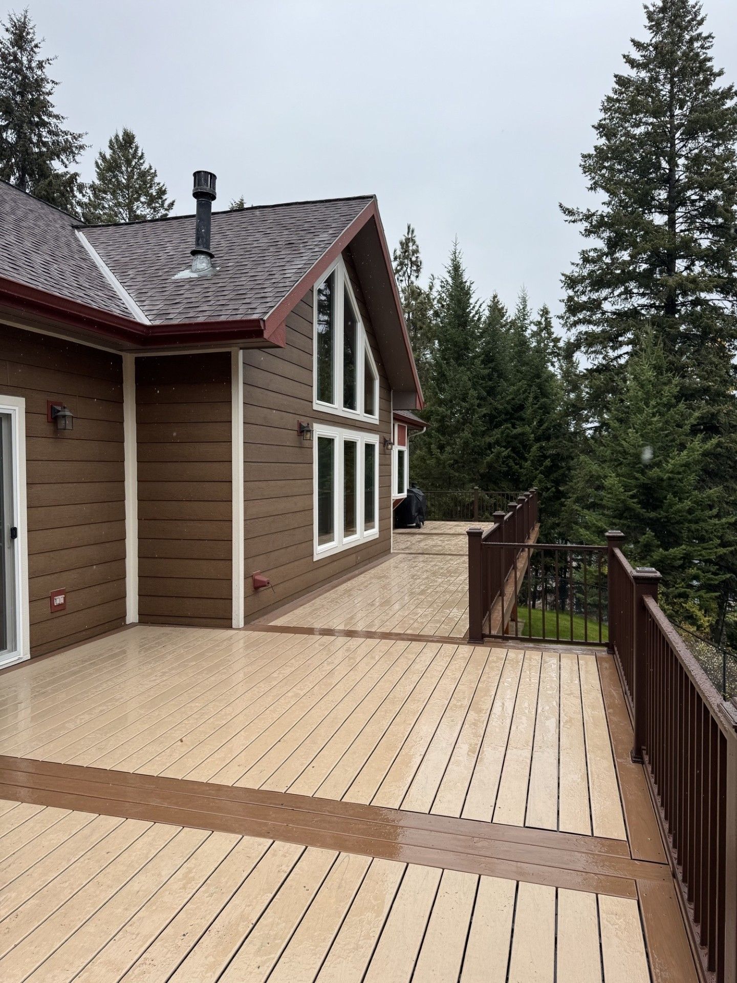 Wooden house deck with railings overlooking evergreen trees under an overcast sky