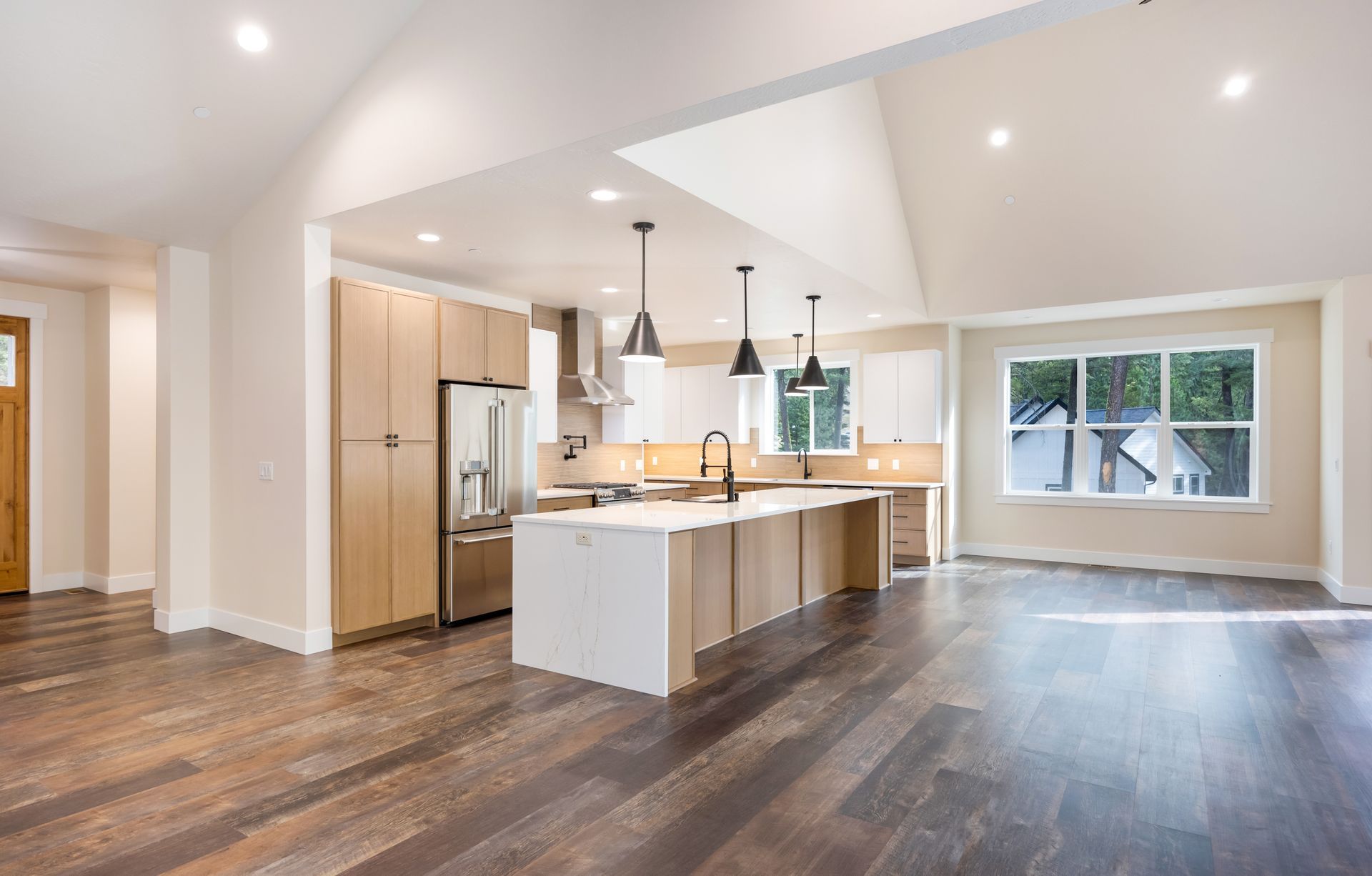 Bright open kitchen with island, wood floors, stainless appliances, and large windows looking out to trees