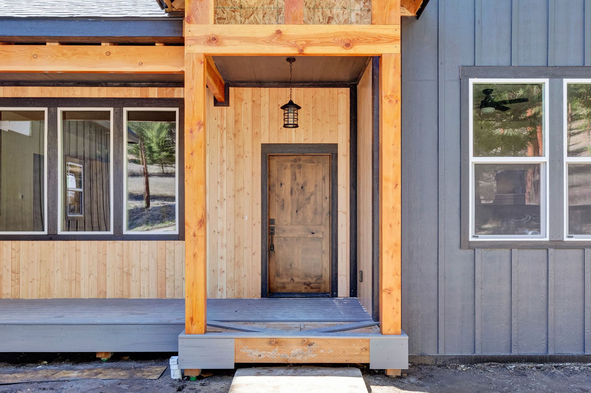 Front entrance of a gray house with wood trim and a wooden door under a covered porch