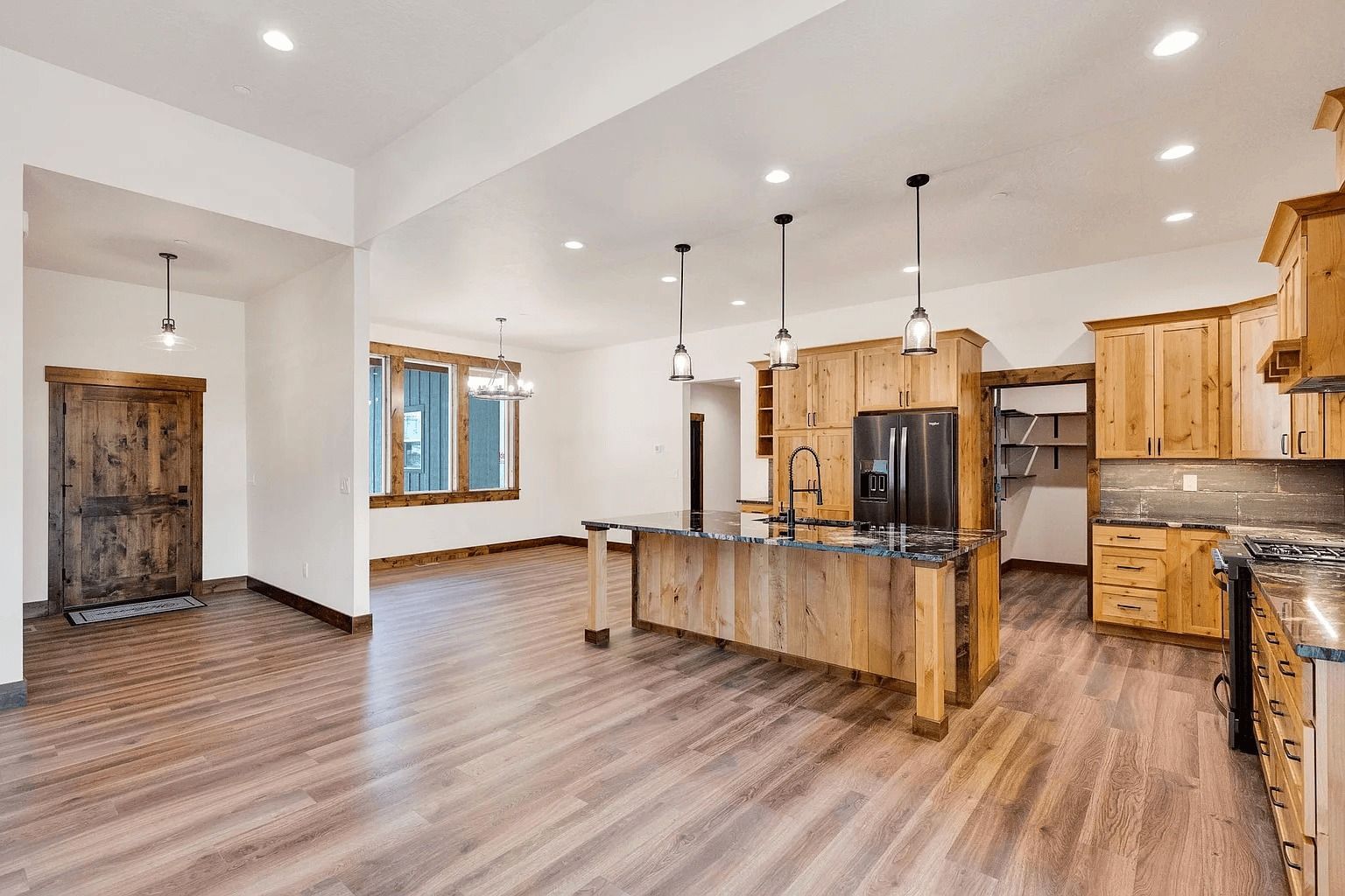 Open-plan kitchen with wood cabinets, island, and hardwood floors, viewed from a bright living area