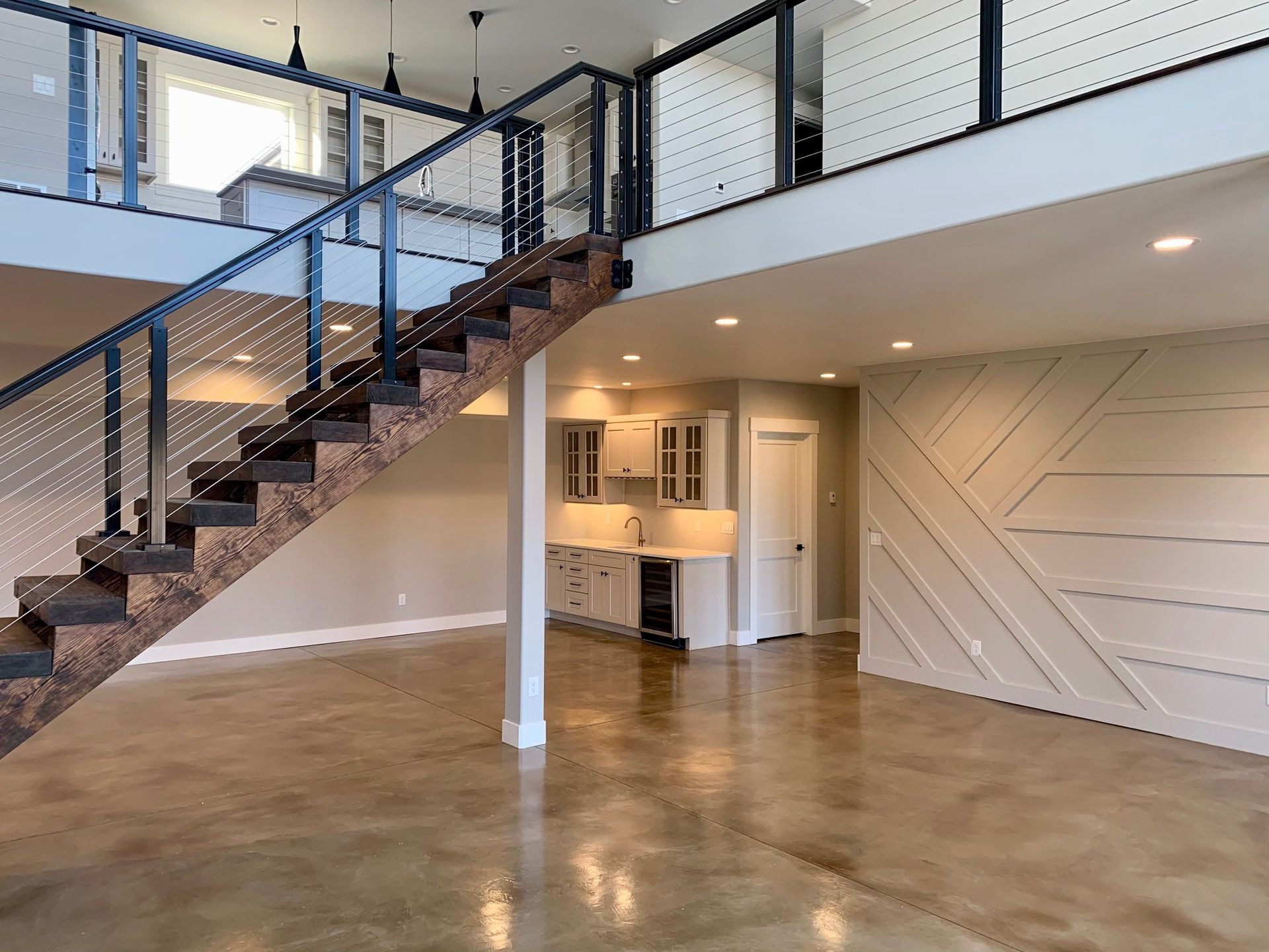 Empty modern loft with open staircase, polished concrete floor, and white accent wall.