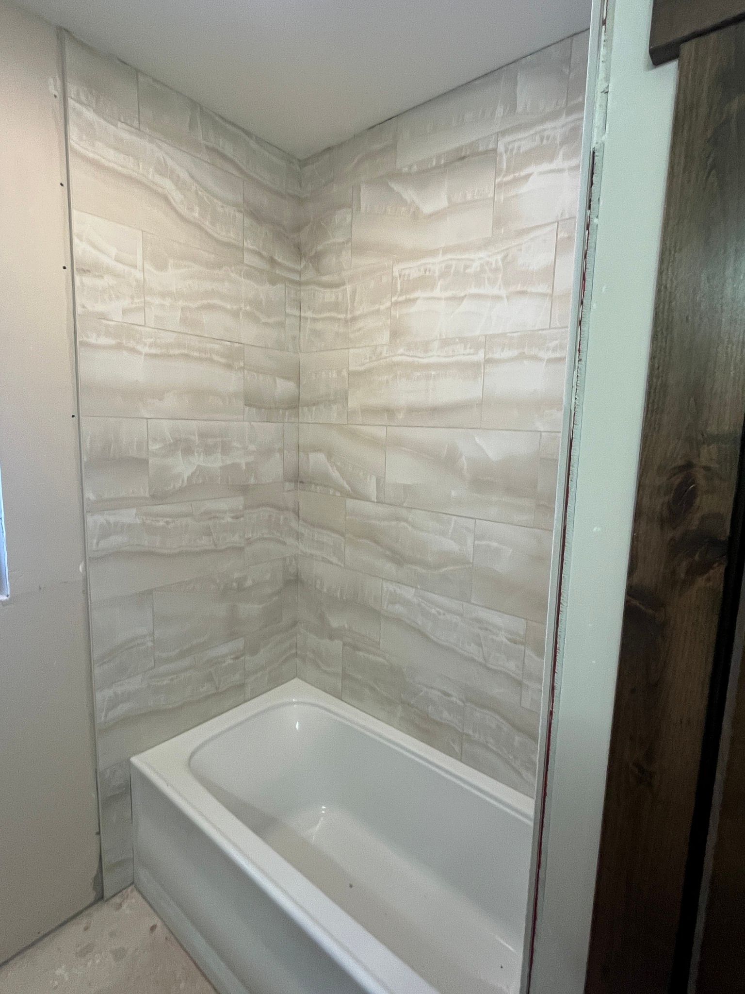 Empty modern bathroom shower with stone-look tiled walls and a white tub.