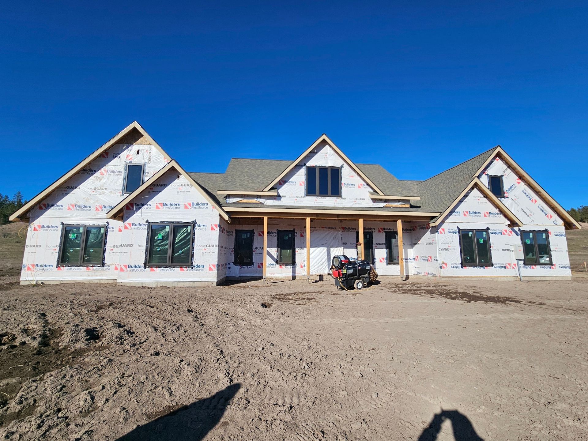 Partially built house under construction with white wrap and a dirt lot under a clear blue sky