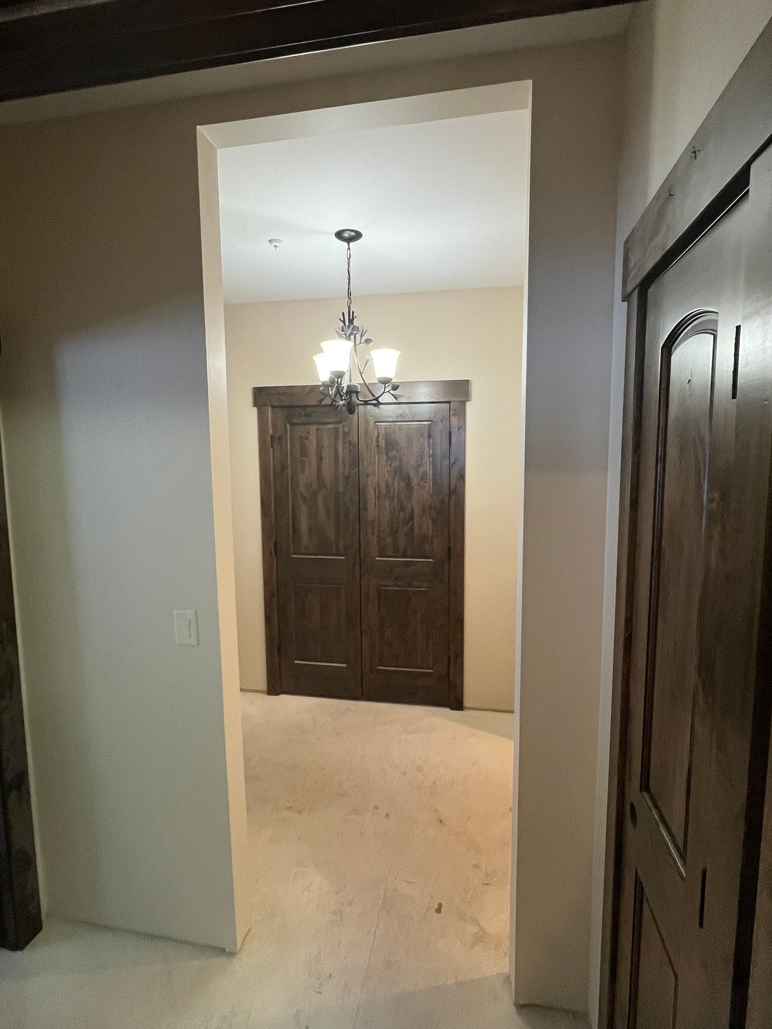 Hallway view into a bright room with a chandelier and dark wood double doors.